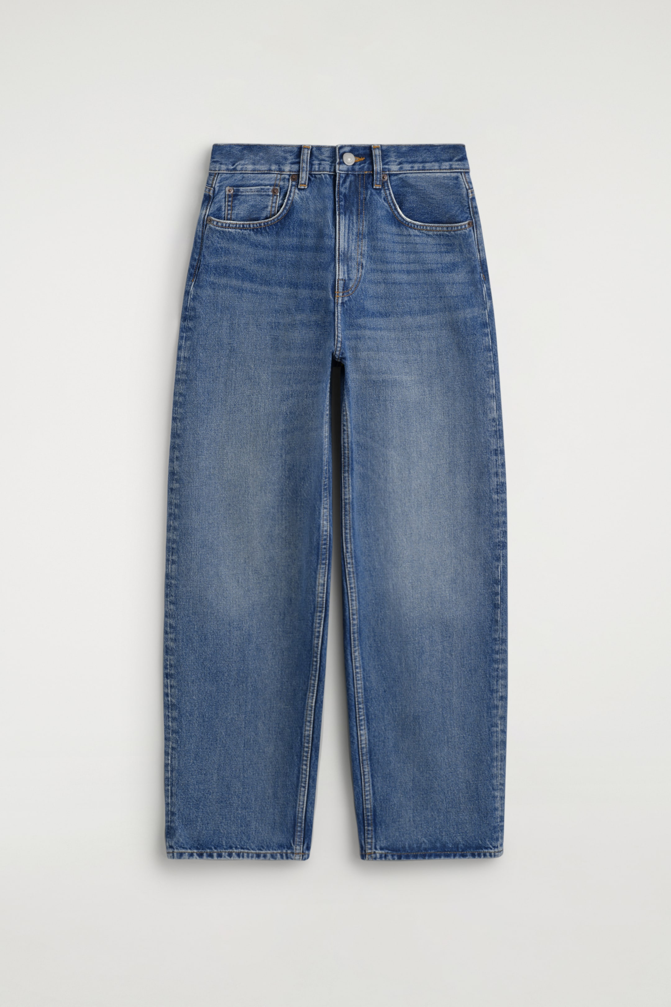 Größeres Bild ansehen: Ein Paar blaue Denim-Jeans liegt flach aus und zeigt die Vorderansicht mit Bund, Gürtelschlaufen sowie Knopf- und Reißverschluss. Sie verfügen über klassische, abgerundete Fronttaschen mit Nieten und eine lässige, gerade Passform mit leichter Auswaschung an den Oberschenkeln.