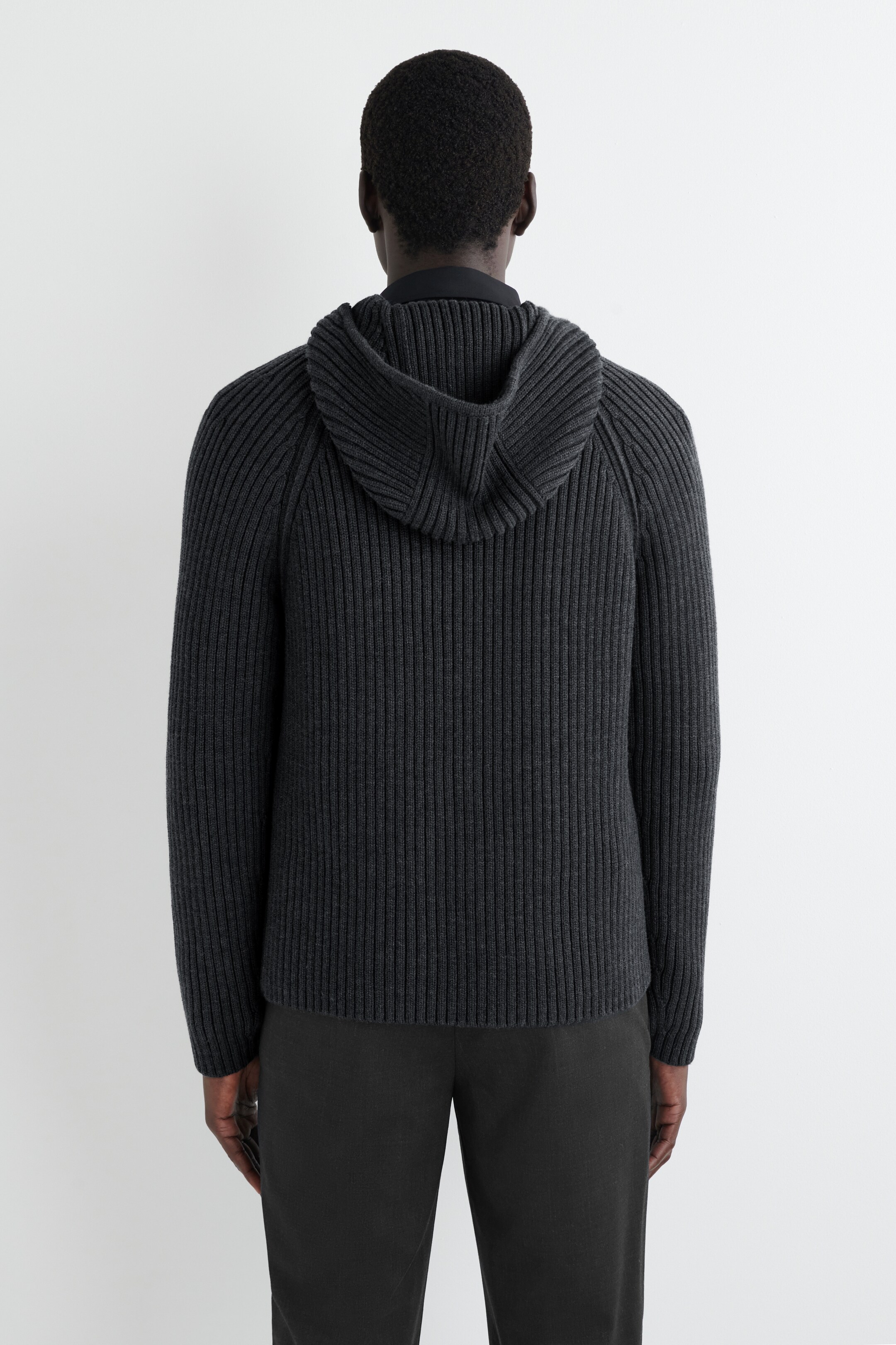 Agrandir l'image: Un pull à capuche côtelé gris foncé est montré de dos, comprenant un tricot côtelé vertical, des manches raglan et une capuche intégrée par-dessus un col de chemise sombre visible.