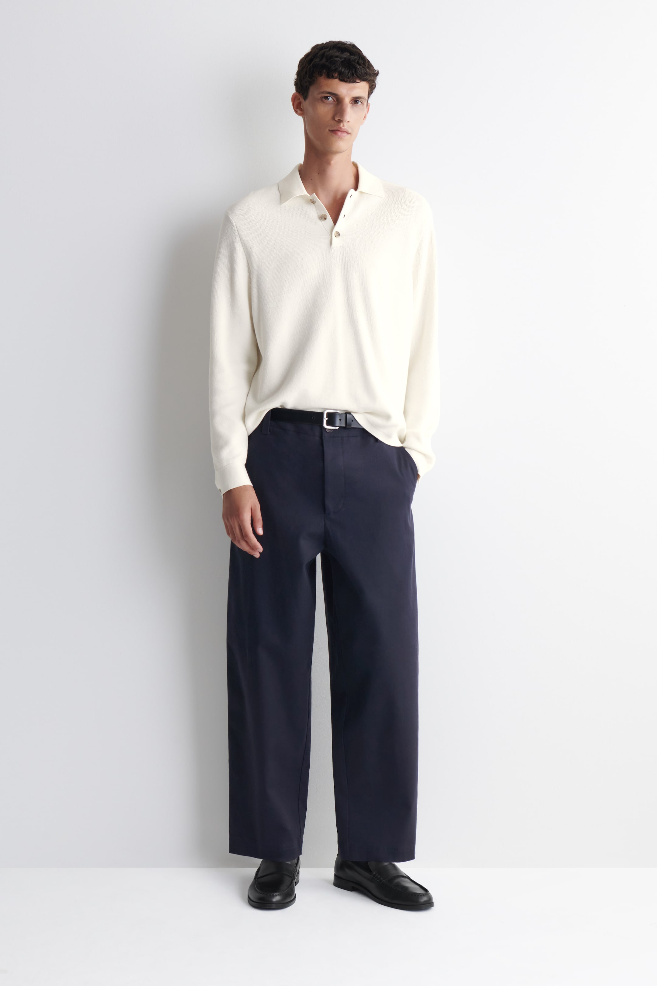 View larger image: An ecru long-sleeved polo shirt is being presented, featuring a textured knit, a polo collar, a three-button placket with light brown buttons, and a relaxed fit, worn untucked.