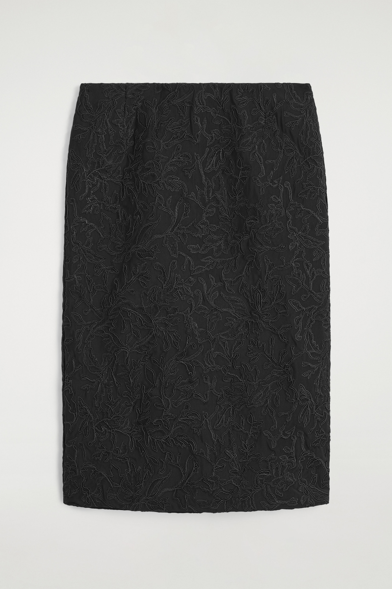 A black midi skirt is shown from the front, showcasing intricate tonal floral embroidery that covers the entire surface of its straight-cut design.