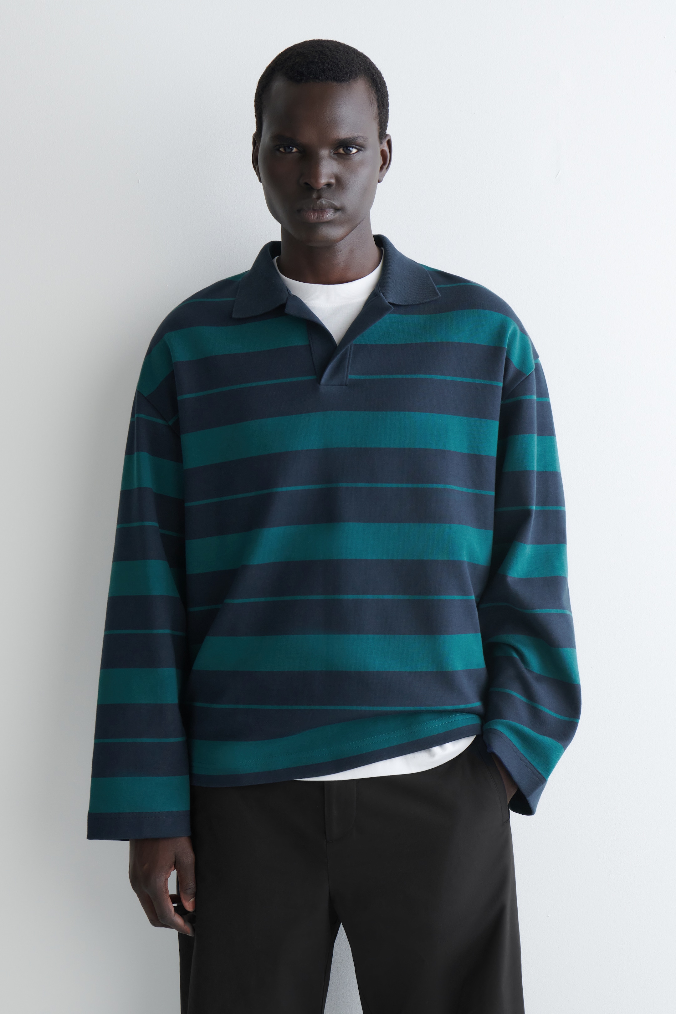 Ver imagen más grande: Se presenta una camiseta polo de manga larga desde el frente, con rayas horizontales de diferentes anchos en azul oscuro y verde azulado, un cuello clásico y una abertura en V sin botones, con una camiseta blanca debajo.