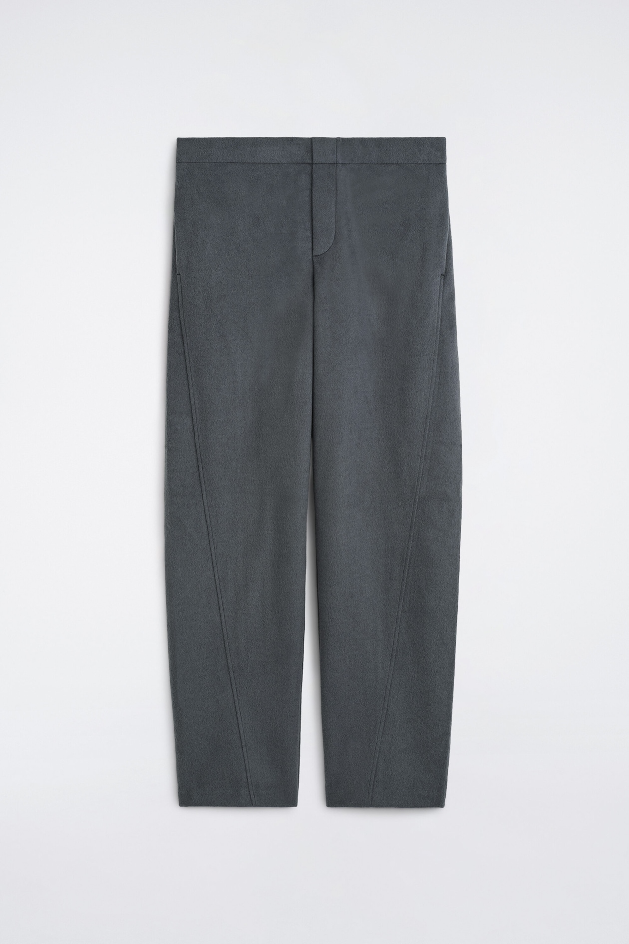 Un pantalon gris foncé est présenté de face, avec une taille épurée, une braguette dissimulée et une silhouette décontractée légèrement fuselée. Le pantalon affiche des coutures obliques marquées qui descendent sur l’avant de chaque jambe, mettant en valeur sa coupe structurée et son tissu texturé.
