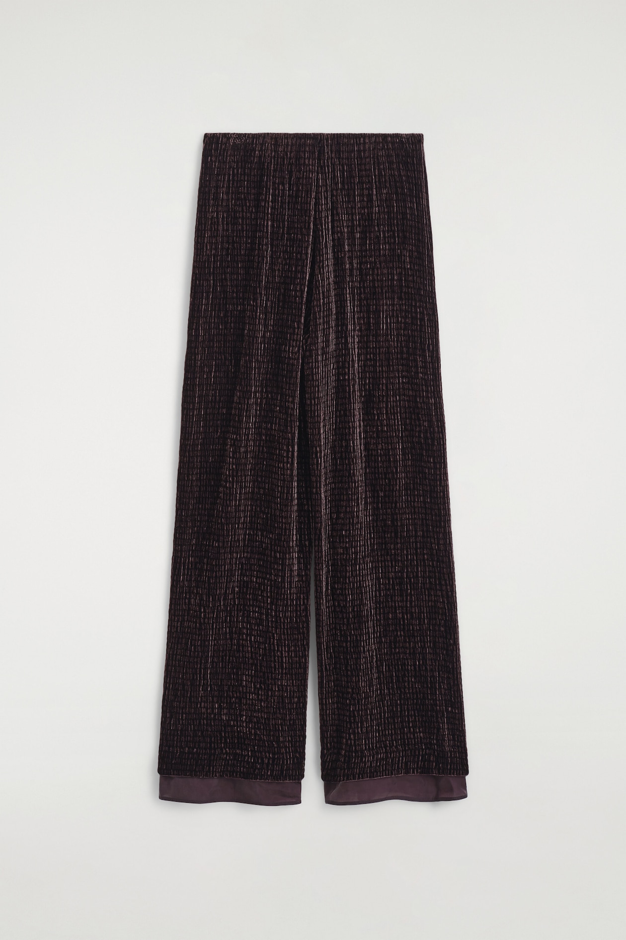 A pair of dark plum wide-leg trousers is hanging straight from a front view, featuring textured, pleated plissé fabric and an elasticized waistband. The trousers are designed with a relaxed fit and finish with a contrasting smooth, tonal satin band at the hem.