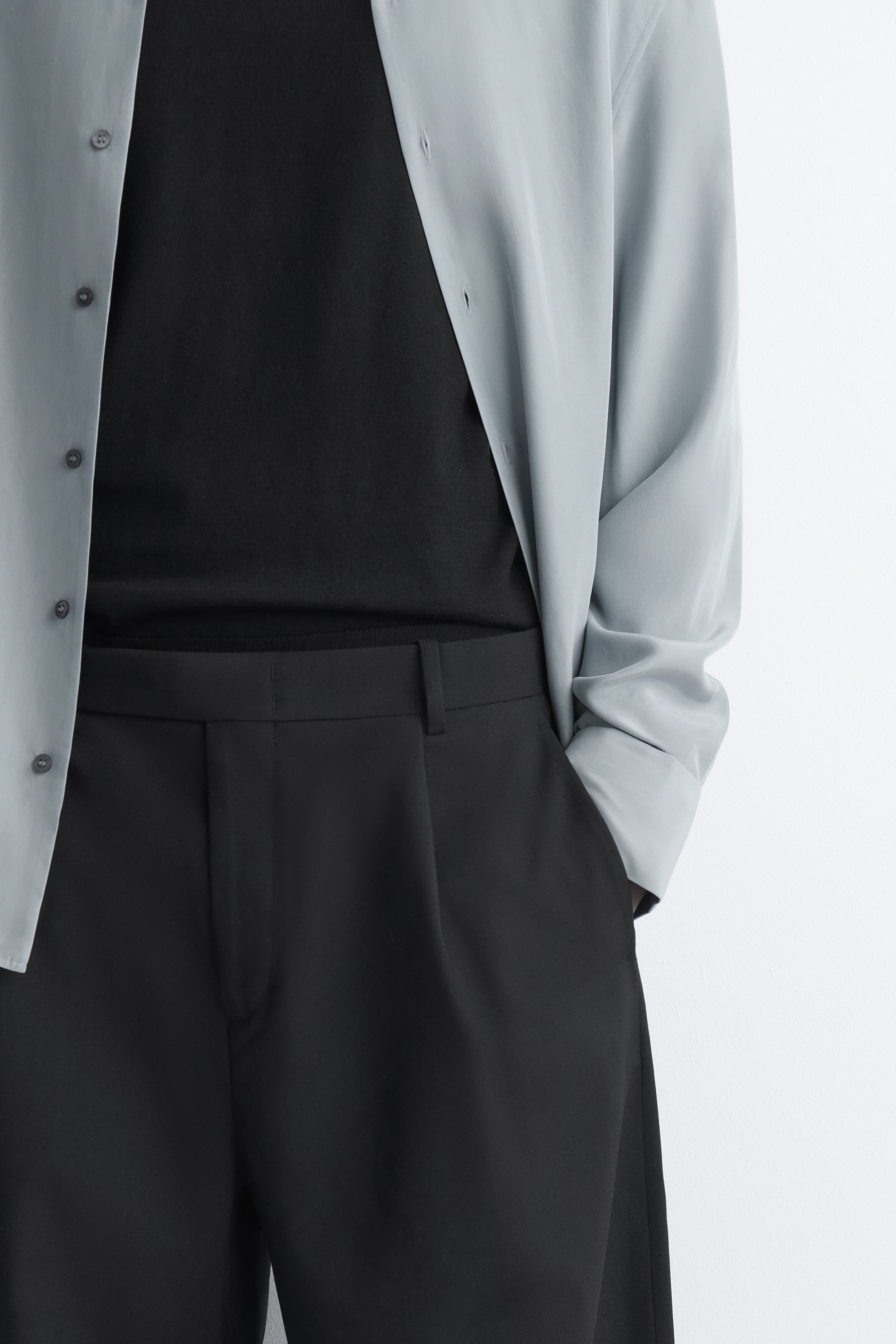 Die BELT-DETAIL WOOL RELAXED-FIT BARREL-LEG PANTS sind in einer Nahaufnahme der vorderen Oberseite zu sehen und zeigen einen strukturierten Bund mit Gürtelschlaufen, dezente Bundfalten sowie eine seitliche Eingrifftasche, in der eine Hand ruht. Die locker geschnittene schwarze Hose wird mit einem in den Bund gesteckten schwarzen Oberteil und einem offen getragenen, hellblauen Langarmhemd kombiniert. Die BELT-DETAIL WOOL RELAXED-FIT BARREL-LEG PANTS sind in einer Nahaufnahme der vorderen Oberseite zu sehen und zeigen einen strukturierten Bund mit Gürtelschlaufen, dezente Bundfalten sowie eine seitliche Eingrifftasche, in der eine Hand ruht. Die locker geschnittene schwarze Hose wird mit einem in den Bund gesteckten schwarzen Oberteil und einem offen getragenen, hellblauen Langarmhemd kombiniert.