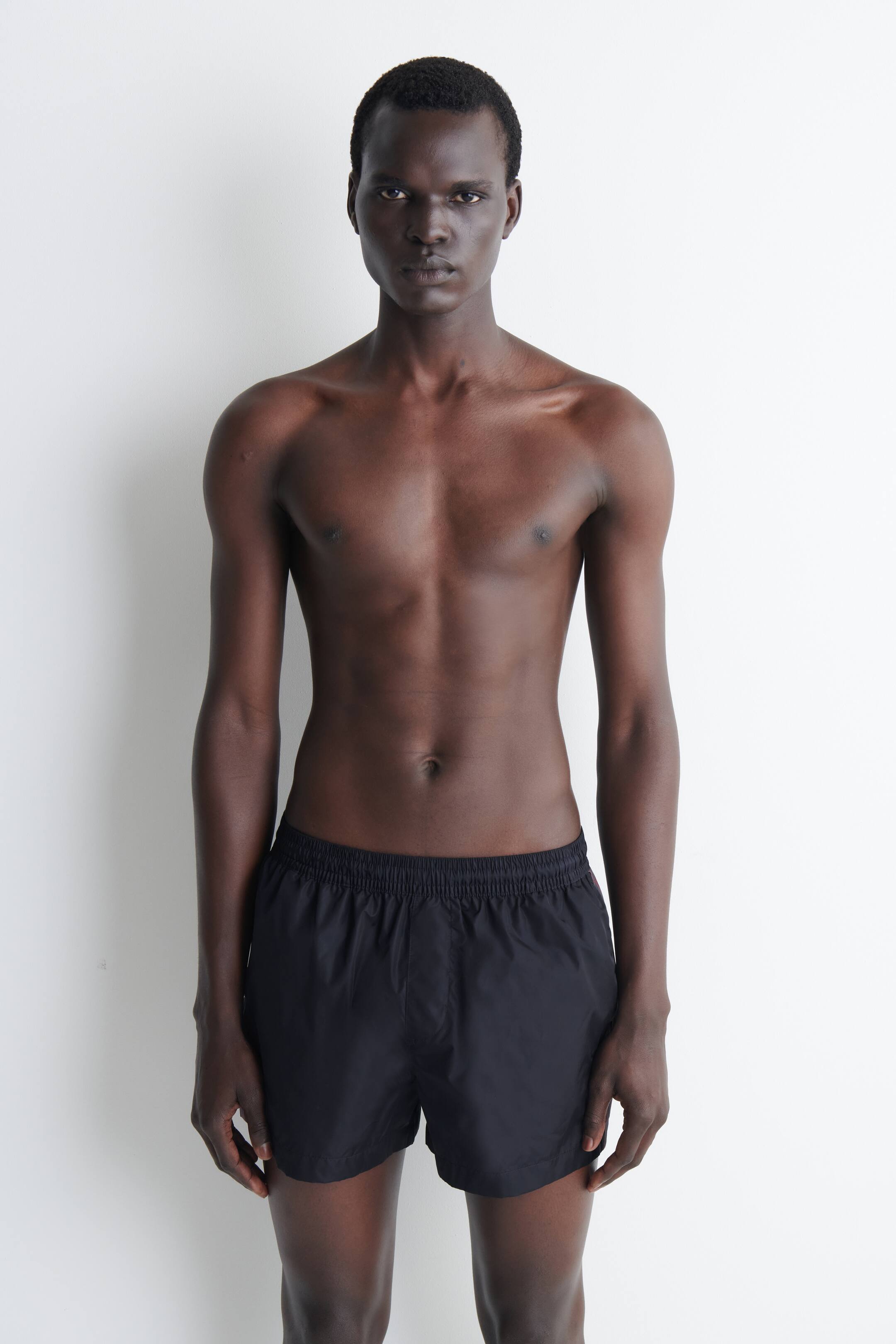 Visualizza immagine più grande: I pantaloncini neri presentano una cintura elasticizzata e una vestibilità rilassata, realizzati in un tessuto leggero, e sono mostrati in una vista frontale, estendendosi appena sopra le ginocchia.