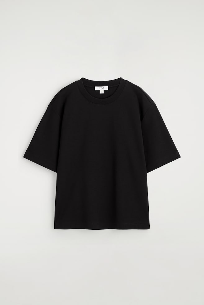 Uma t-shirt preta está a exibir a sua frente, com uma gola redonda canelada, mangas curtas e um corte descontraído. - 1