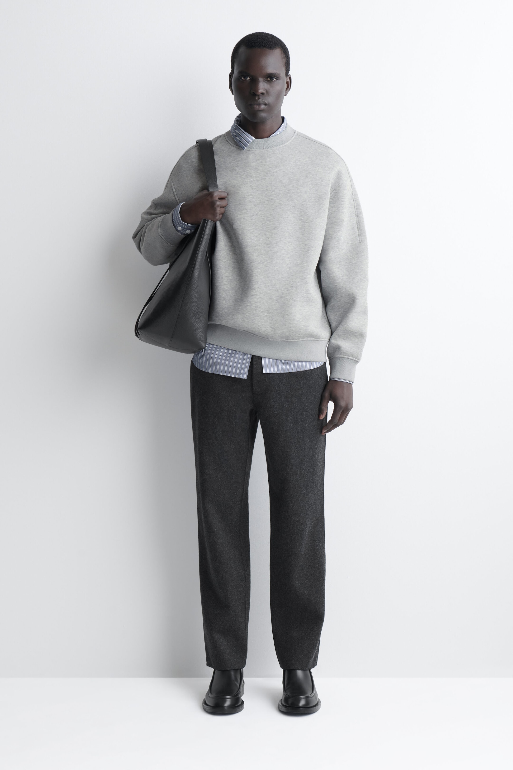 The relaxed scuba sweatshirt in light grey is shown from the front, featuring a crew neck, dropped shoulders, and ribbed detailing on the cuffs and hem. It is layered over a striped collared shirt, which is visible at the neck, cuffs, and hem. The relaxed scuba sweatshirt in light grey is shown from the front, featuring a crew neck, dropped shoulders, and ribbed detailing on the cuffs and hem. It is layered over a striped collared shirt, which is visible at the neck, cuffs, and hem.