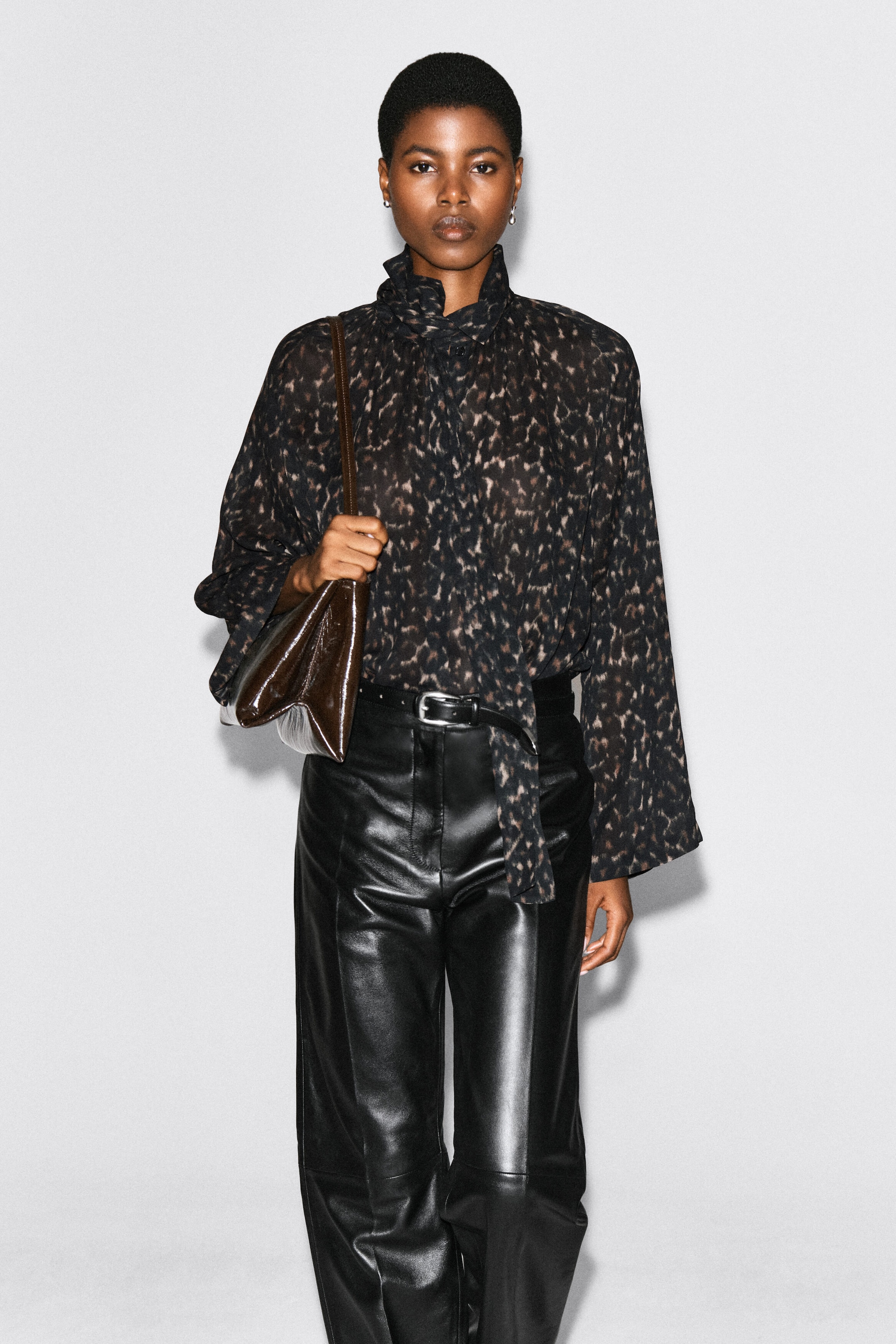 A leopard-print fluid top featuring a high scarf-detail collar and long, wide sleeves is worn by the model. The top is tucked into black leather trousers with a belt, and a brown shoulder bag is carried on the shoulder. A leopard-print fluid top featuring a high scarf-detail collar and long, wide sleeves is worn by the model. The top is tucked into black leather trousers with a belt, and a brown shoulder bag is carried on the shoulder.
