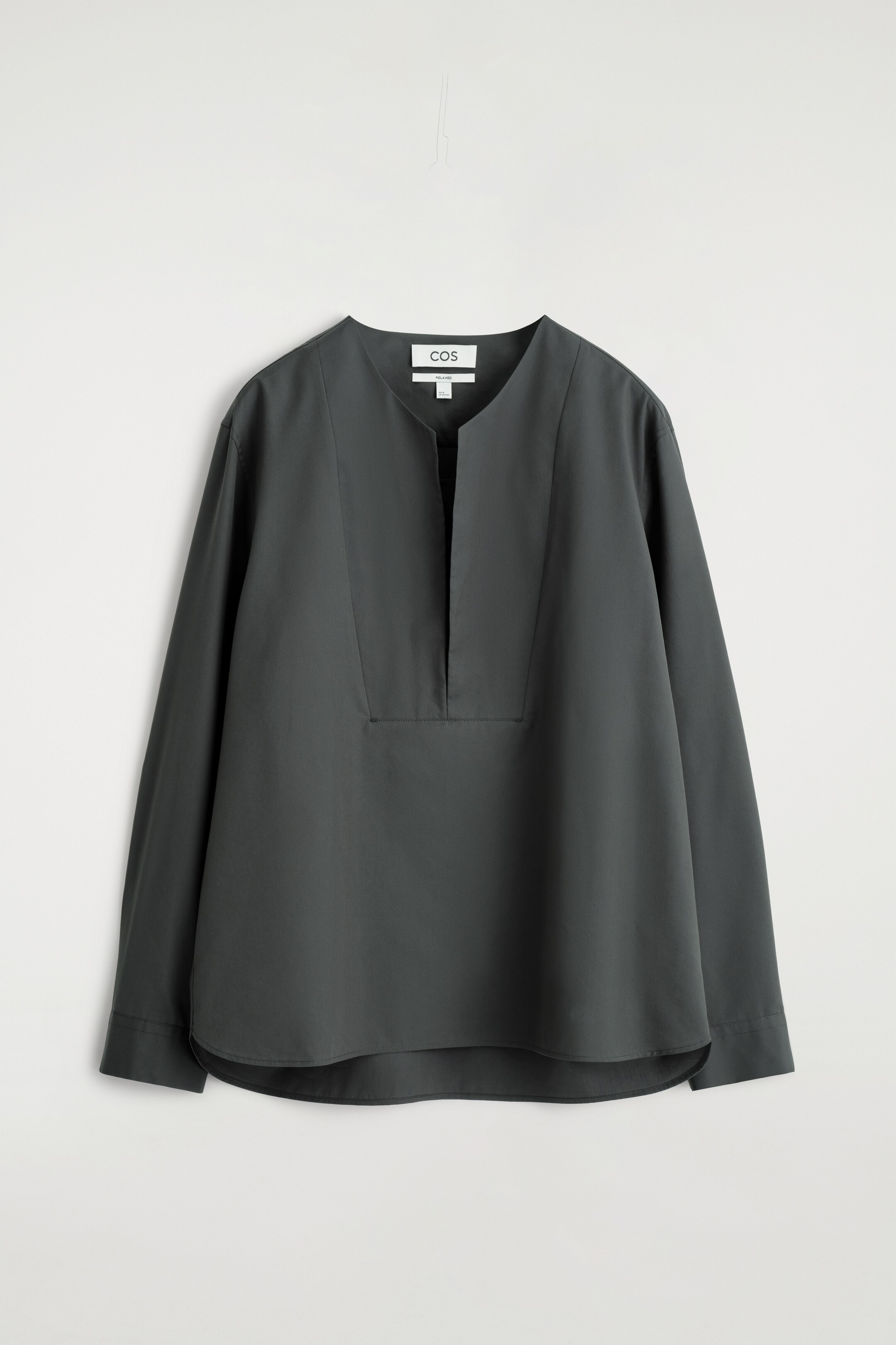 Ver imagen más grande: Una camisa túnica de color gris oscuro se presenta desde el frente, con un escote en V sin cuello y una tapeta corta y cosida. Muestra mangas largas de corte relajado y un dobladillo curvado.