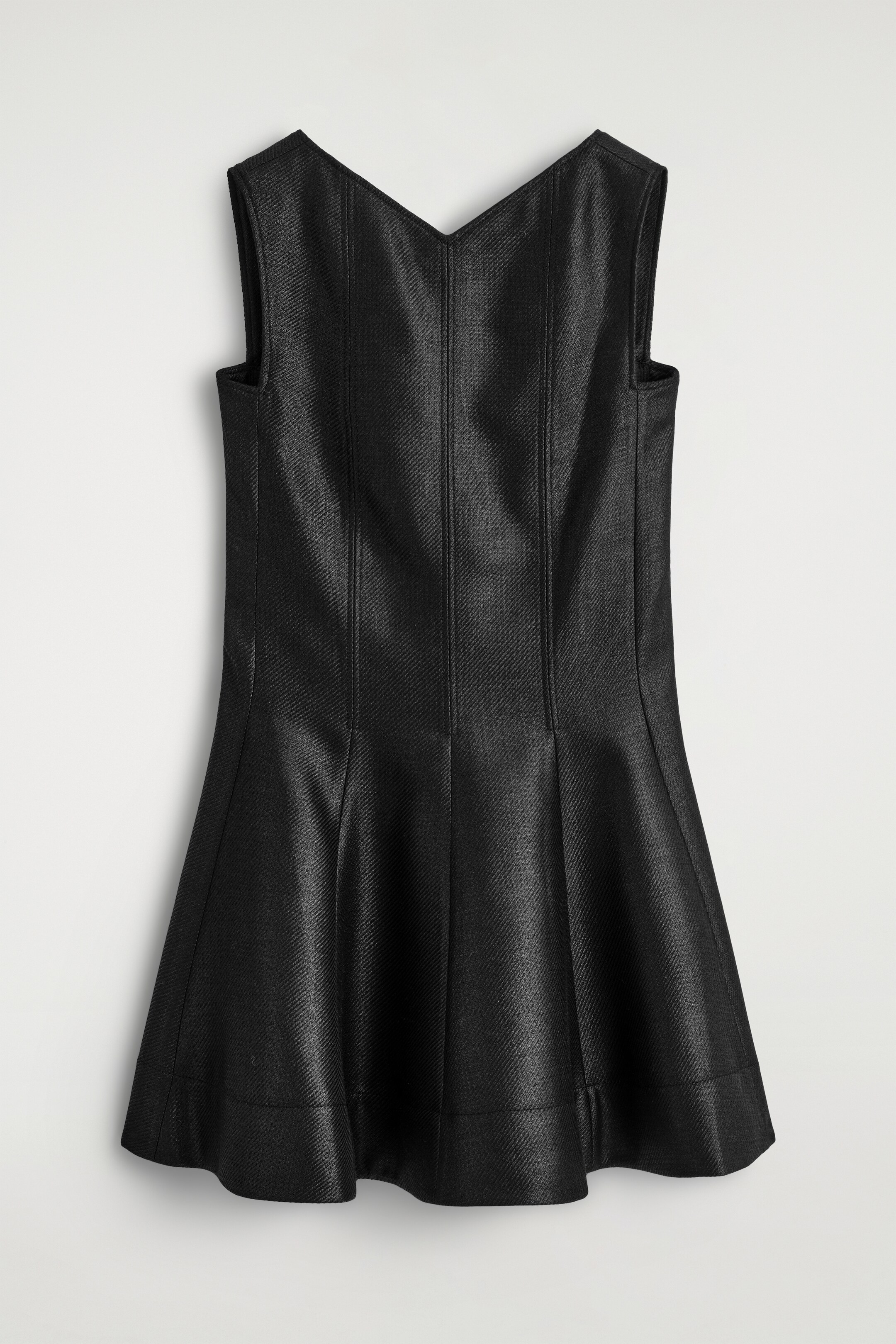 Agrandir l'image: Une robe noire sans manches présente son dos, avec un décolleté en V et des coutures verticales le long du corsage. La jupe s'évase depuis la taille avec des plis visibles, et le tissu présente un tissage en diagonale subtil.