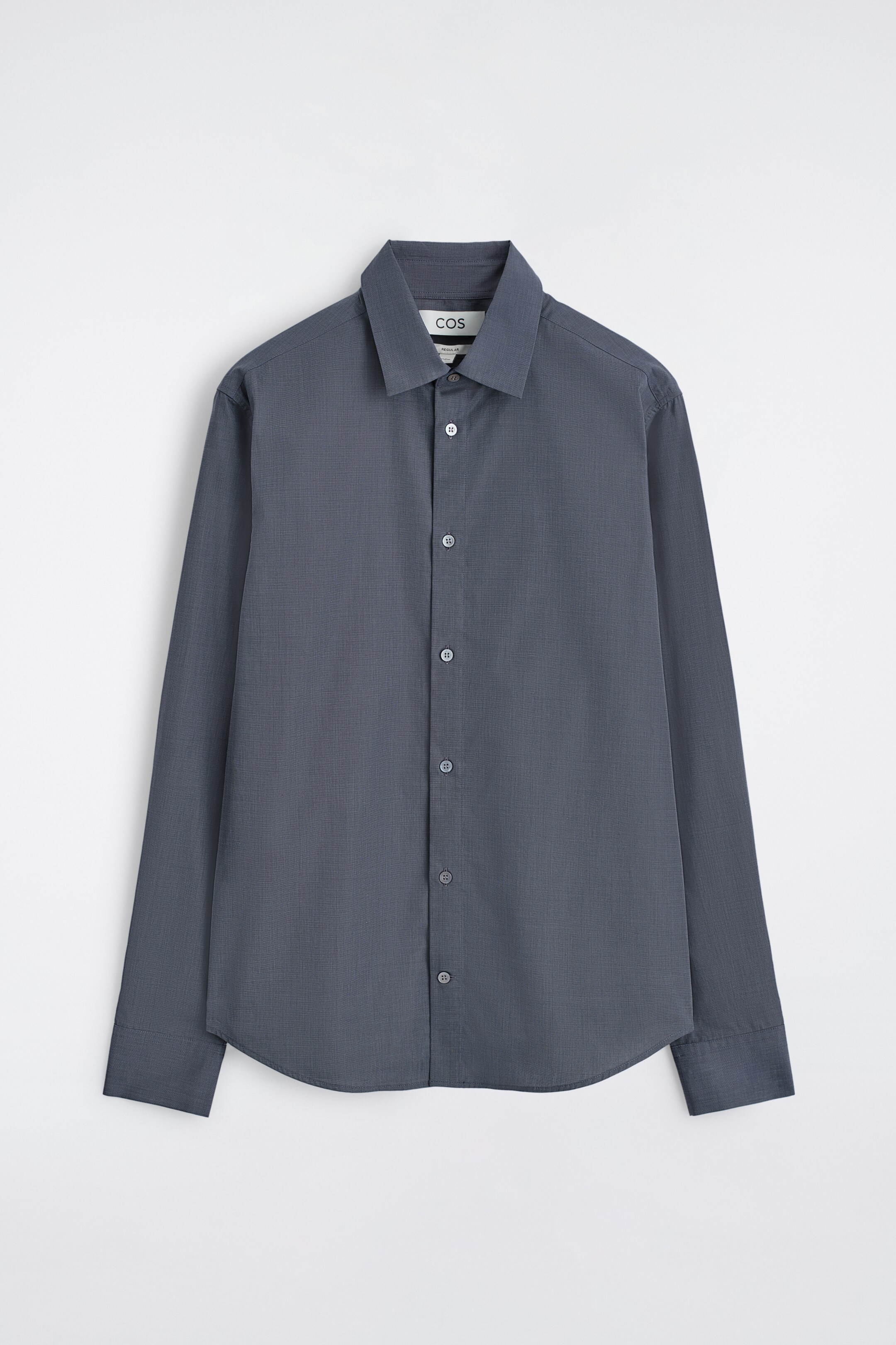Agrandir l'image: Une chemise à manches longues gris foncé est présentée de face, avec un tissage texturé subtil. Elle a un col pointu, une fermeture à boutons sur le devant avec des boutons de couleur claire, et des poignets à bouton unique.