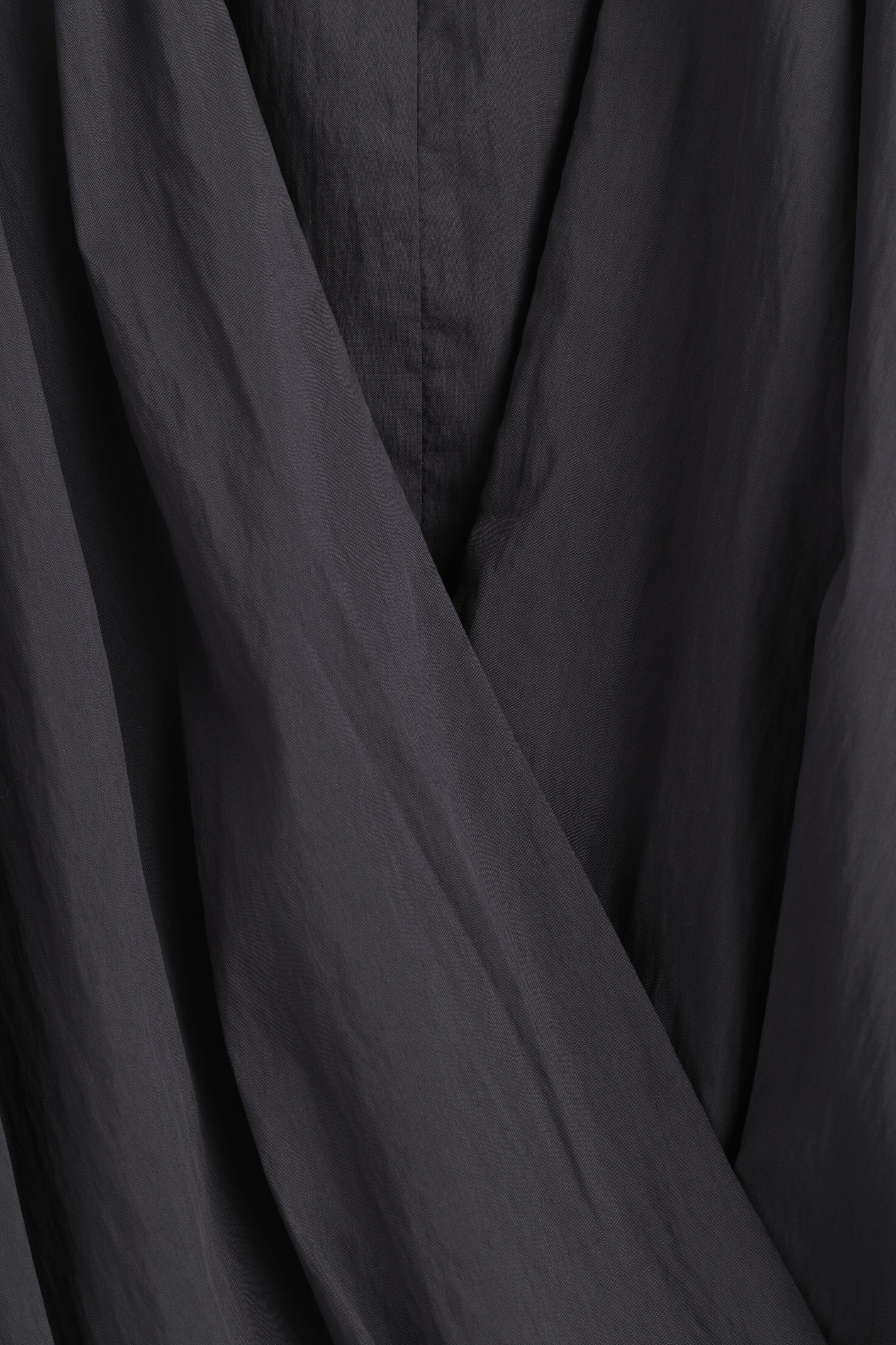 Agrandir l'image: La blouse gris foncé présente un gros plan de son devant portefeuille, où des couches délicates d'organza se tordent en plis diagonaux prononcés. Une couture verticale subtile traverse le centre du tissu.