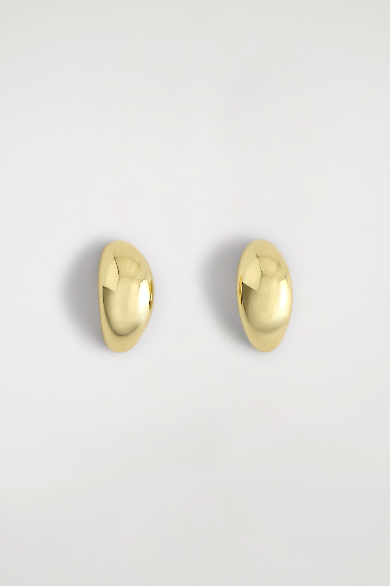 Les boucles d’oreilles demi-créoles sculpturales présentent un design bombé, arrondi et massif, avec une finition dorée très polie. La paire est orientée de face, mettant en valeur leurs surfaces lisses et réfléchissantes ainsi que leurs contours courbés.