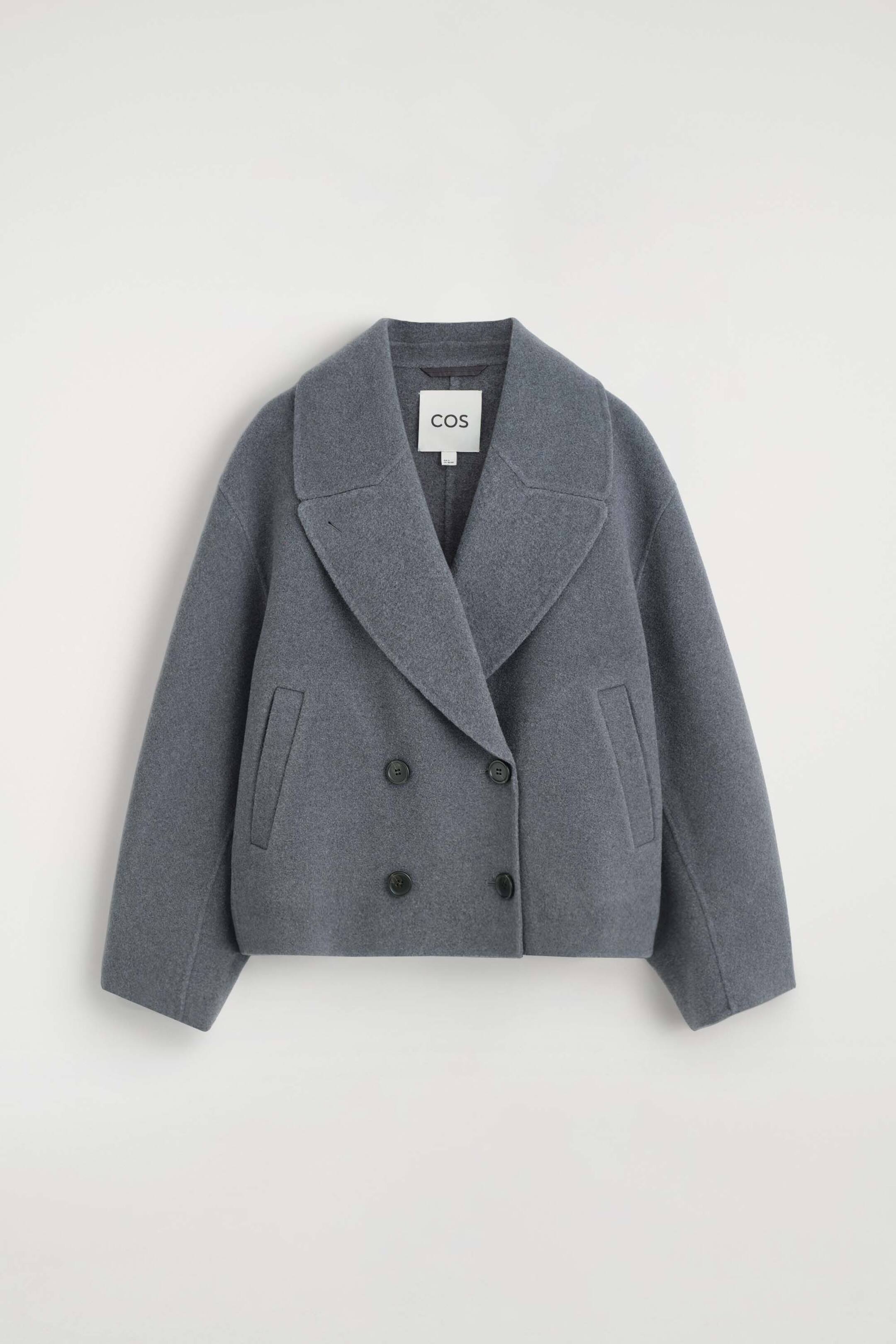 Agrandir l'image: Une veste en laine oversize double face, dans une teinte gris moyen, est vue de face, mettant en valeur une coupe croisée à double boutonnage avec quatre boutons foncés et de larges revers crantés. La veste présente des épaules tombantes, des manches amples et des poches passepoilées inclinées de chaque côté.