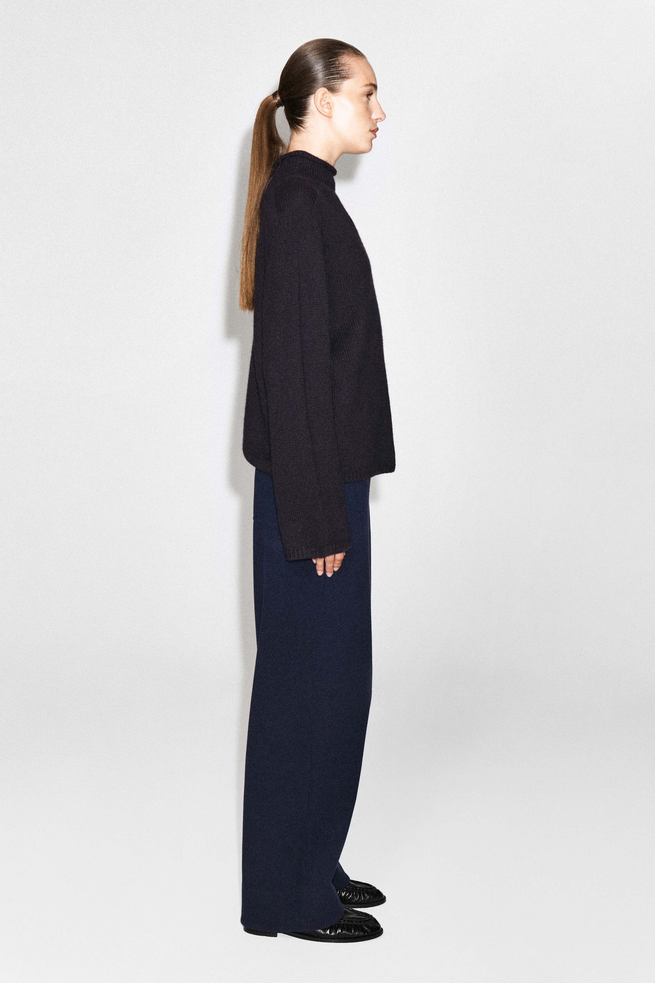 Le mannequin, photographié de profil, porte un pantalon large en velours côtelé bleu marine foncé et jersey. Le pantalon fluide à coupe décontractée est agencé avec un chandail noir en tricot à col montant et des chaussures noires plates. Le mannequin, photographié de profil, porte un pantalon large en velours côtelé bleu marine foncé et jersey. Le pantalon fluide à coupe décontractée est agencé avec un chandail noir en tricot à col montant et des chaussures noires plates.