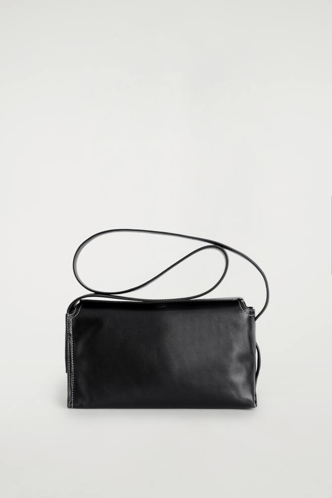 A black crossbody bag is facing FRONT, featuring a fold-over flap and a thin strap that threads through its sides. White contrast stitching is visible along its edges. - 1