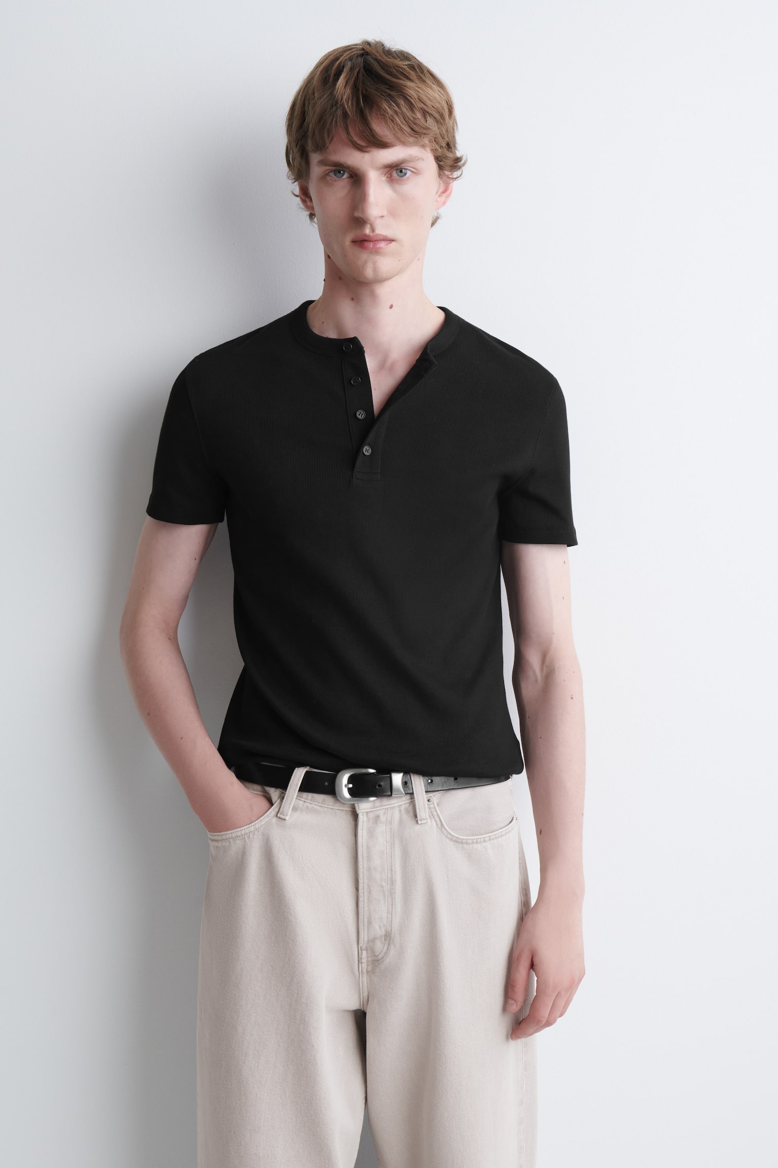 En svart slim fit-ribbestrikket Henley T-skjorte vises forfra, med rund hals og stolpe med fire knapper samt korte ermer. Plagget har en fin ribbestrikket struktur over hele plagget og en ren, rett kant nederst. - 1
