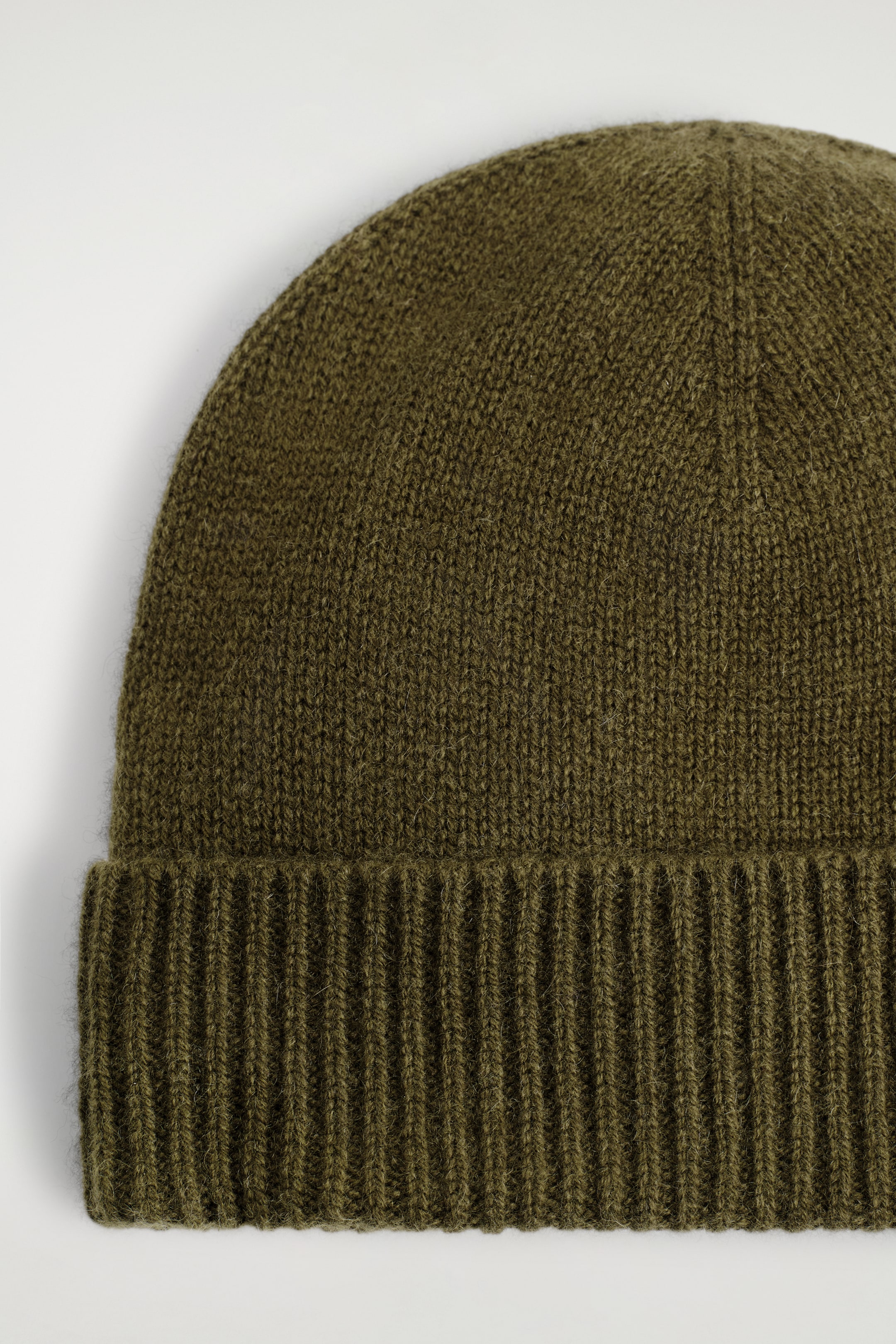 Größeres Bild ansehen: Eine olivgrüne Strickmütze wird von vorne präsentiert, wobei ihr glatter Hauptteil und ein breiter, gerippter umgeschlagener Rand zu sehen sind.