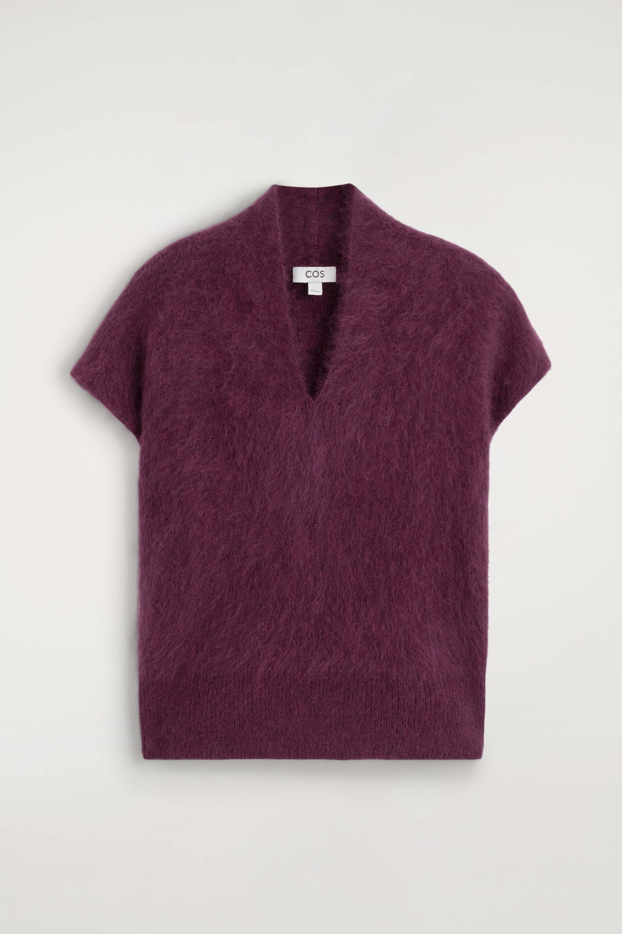 A draped brushed merino wool top in deep plum is laid flat, showing the front view. The top features a fuzzy, brushed texture, a deep V-neckline, short cap sleeves, and a straight hem.
