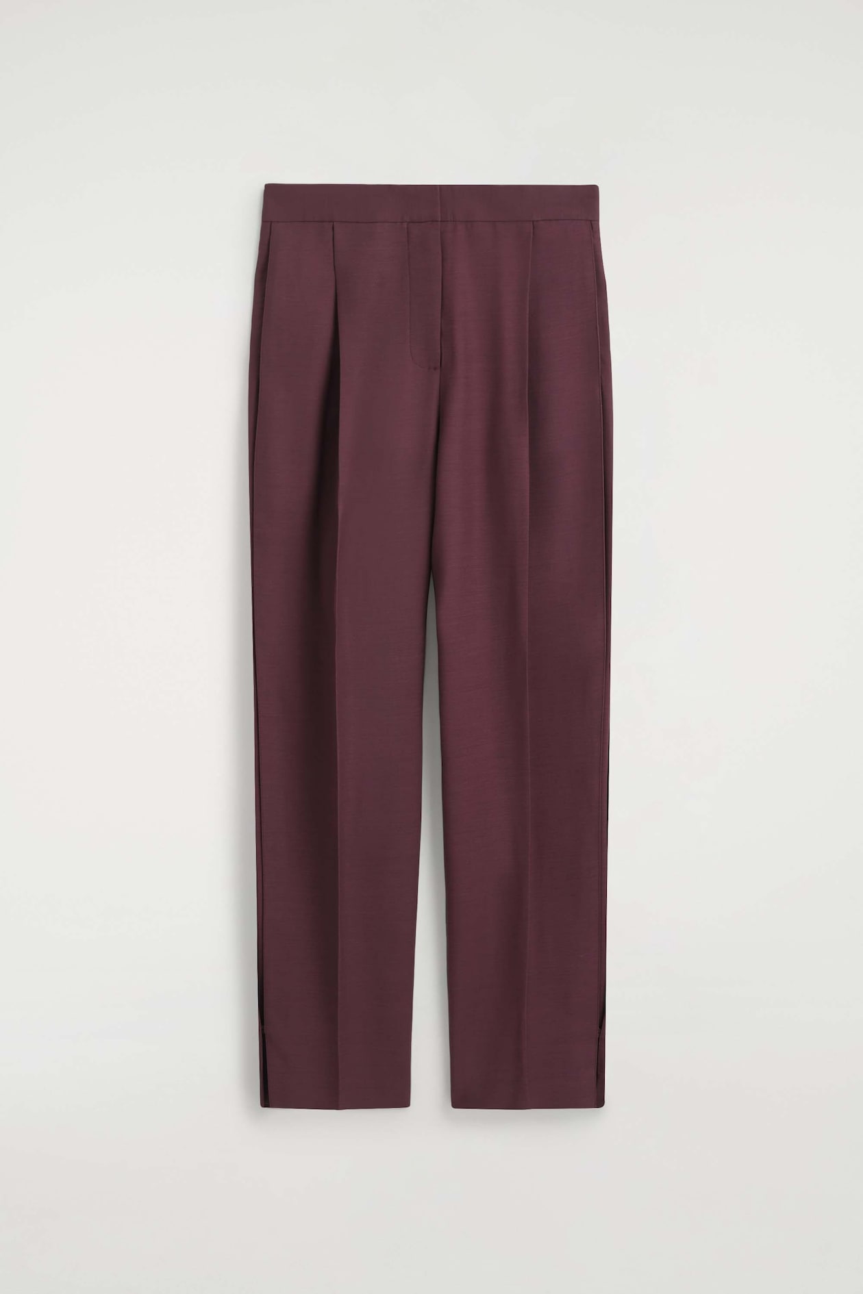 Pleated-panel straight-leg pants in a deep burgundy hue are shown from the front, featuring a clean waistband with a concealed closure. The design features prominent front pleats and sharp pressed creases running down the center of each leg.