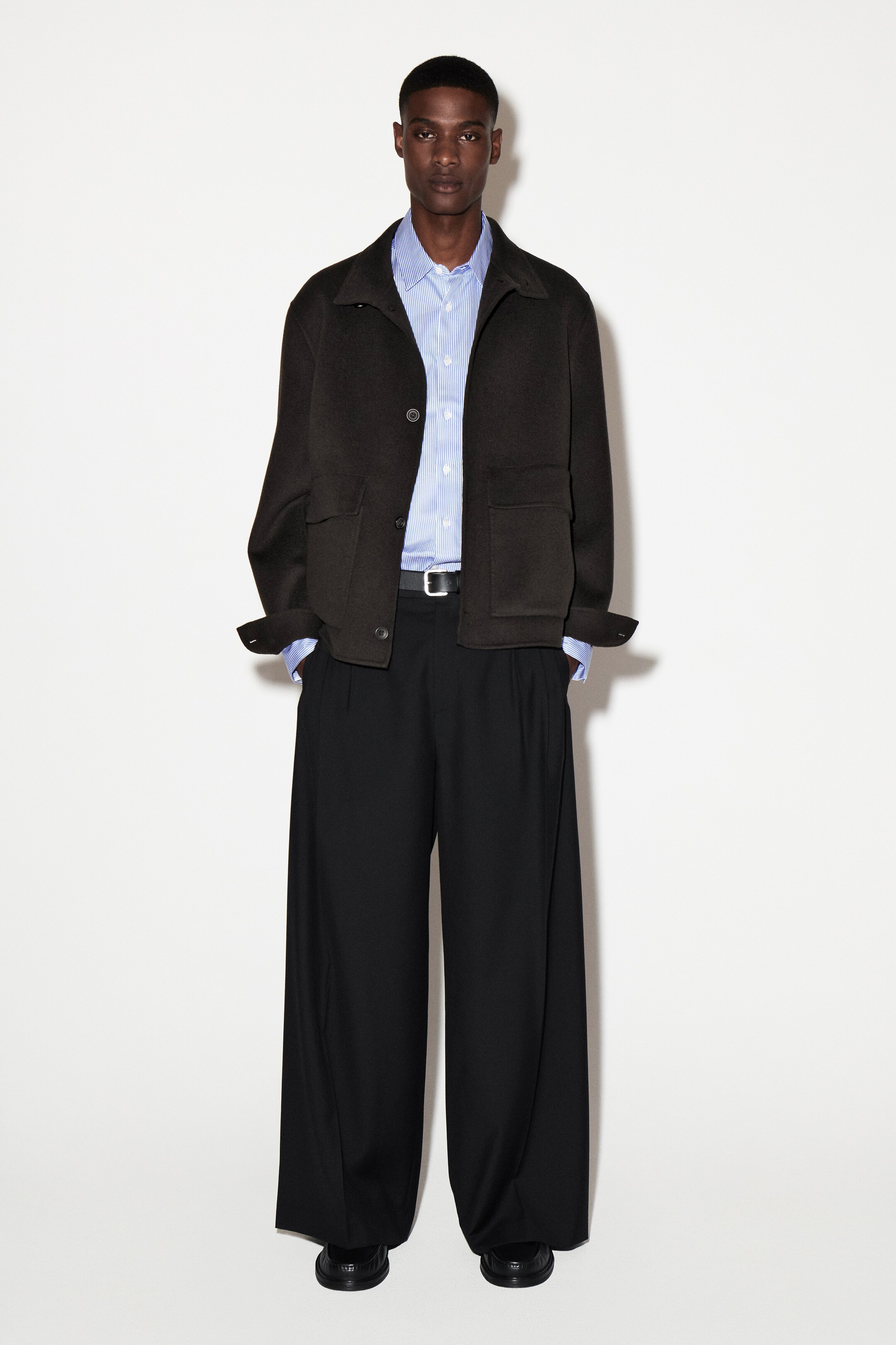 Größeres Bild anzeigen: Ein slim-fit hellblau gestreiftes Popeline-Hemd wird von vorne präsentiert, mit einem spitzen Kragen und Perlmuttknöpfen entlang der Knopfleiste. Die geknöpften langen Ärmel sind sichtbar, die unter einer dunklen Jacke hervorragen.