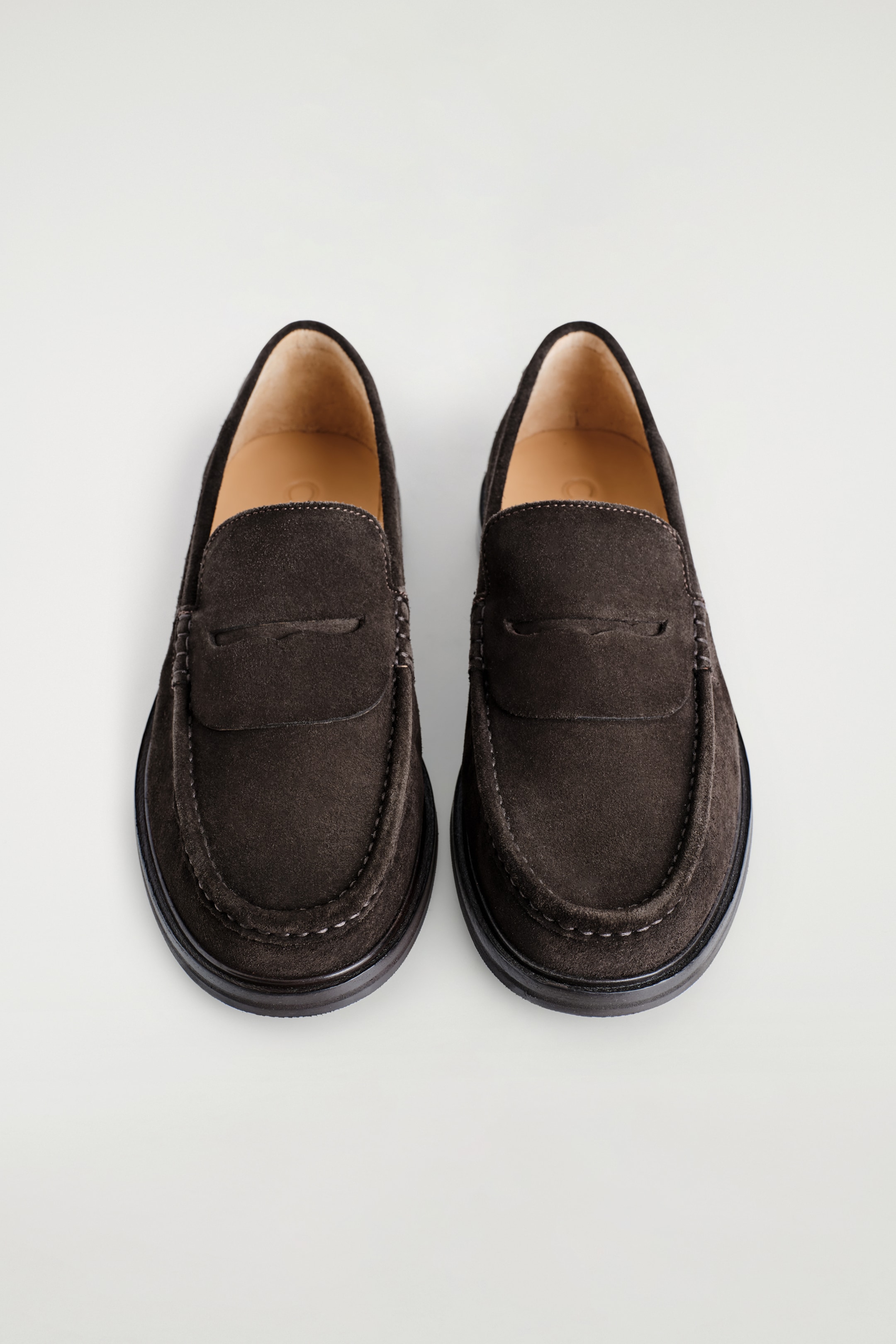 Ver imagem maior: Um par de mocassins de camurça castanho escuro é apresentado de uma vista de cima, com costura tonal em torno do moc toe e uma ranhura clássica para moeda no vamp.