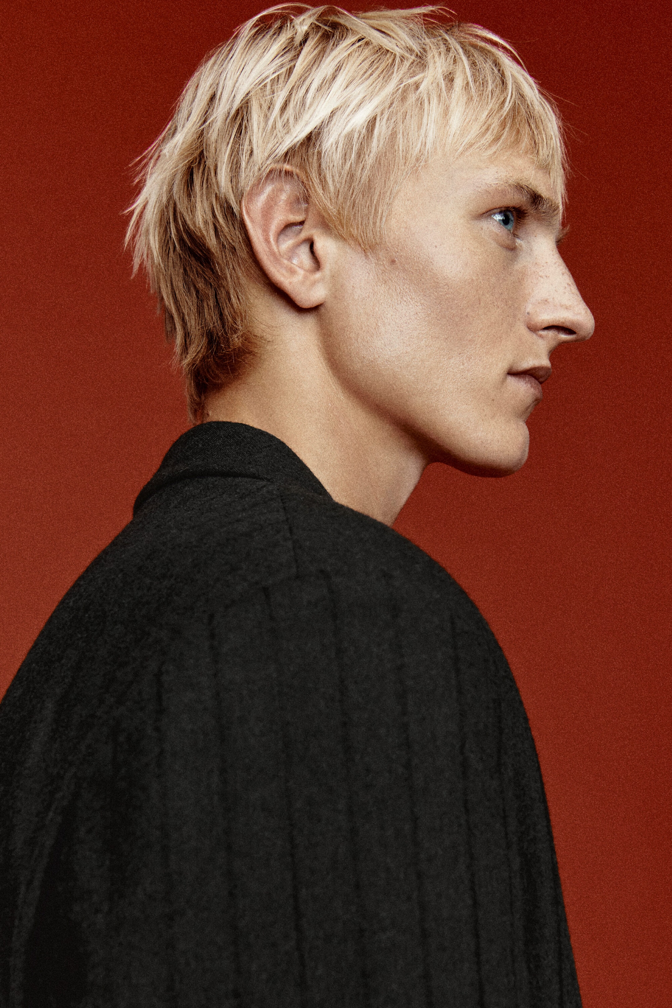 The dark gray pinstriped blazer is shown in side profile, highlighting its textured wool twill fabric, structured shoulders, and collar line.