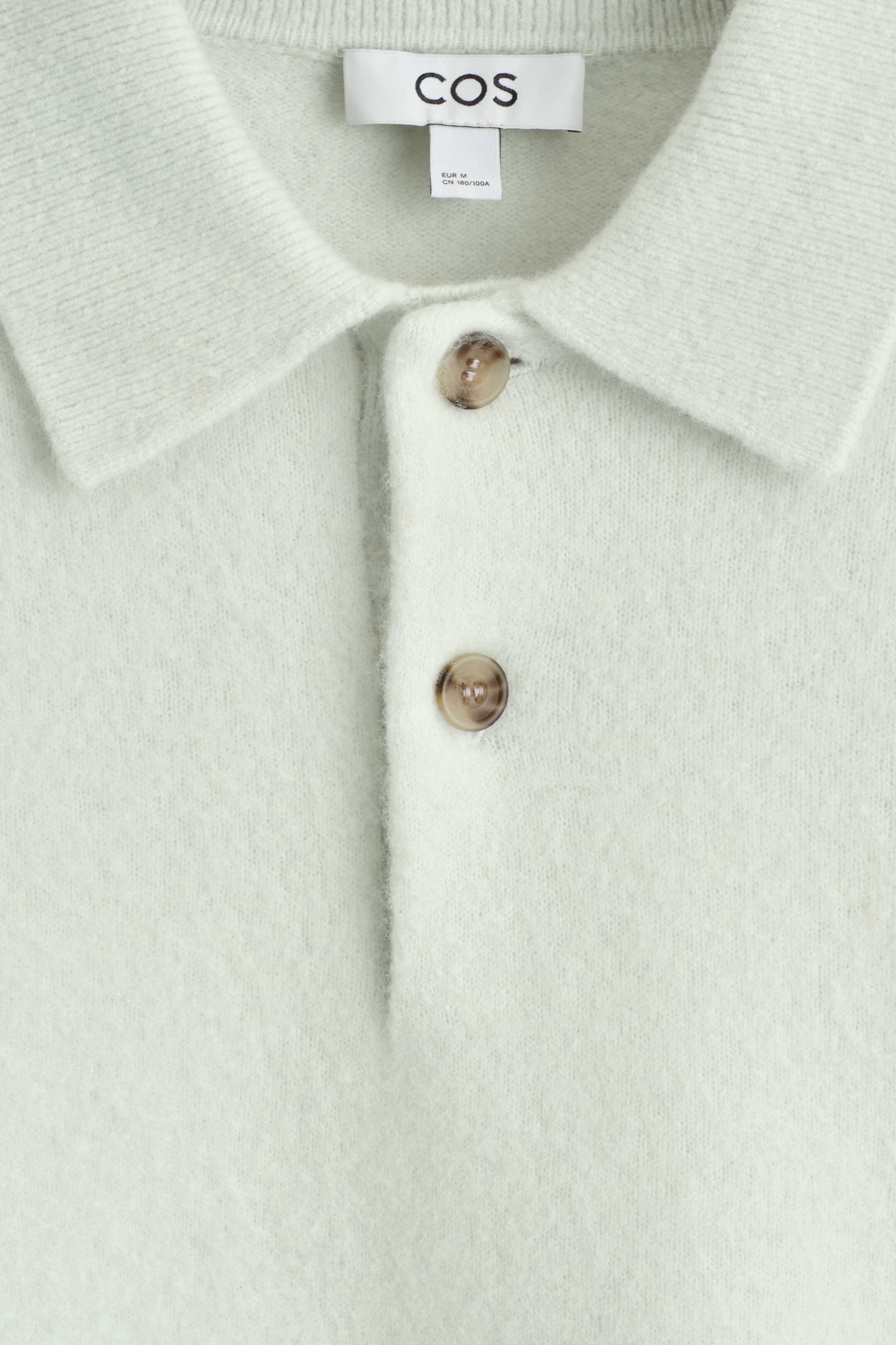 Visualizza immagine più grande: Una polo verde chiaro è mostrata dal davanti, mostrando una texture spazzolata e un colletto classico. La sua abbottonatura a due bottoni presenta bottoni screziati di un marrone chiaro.
