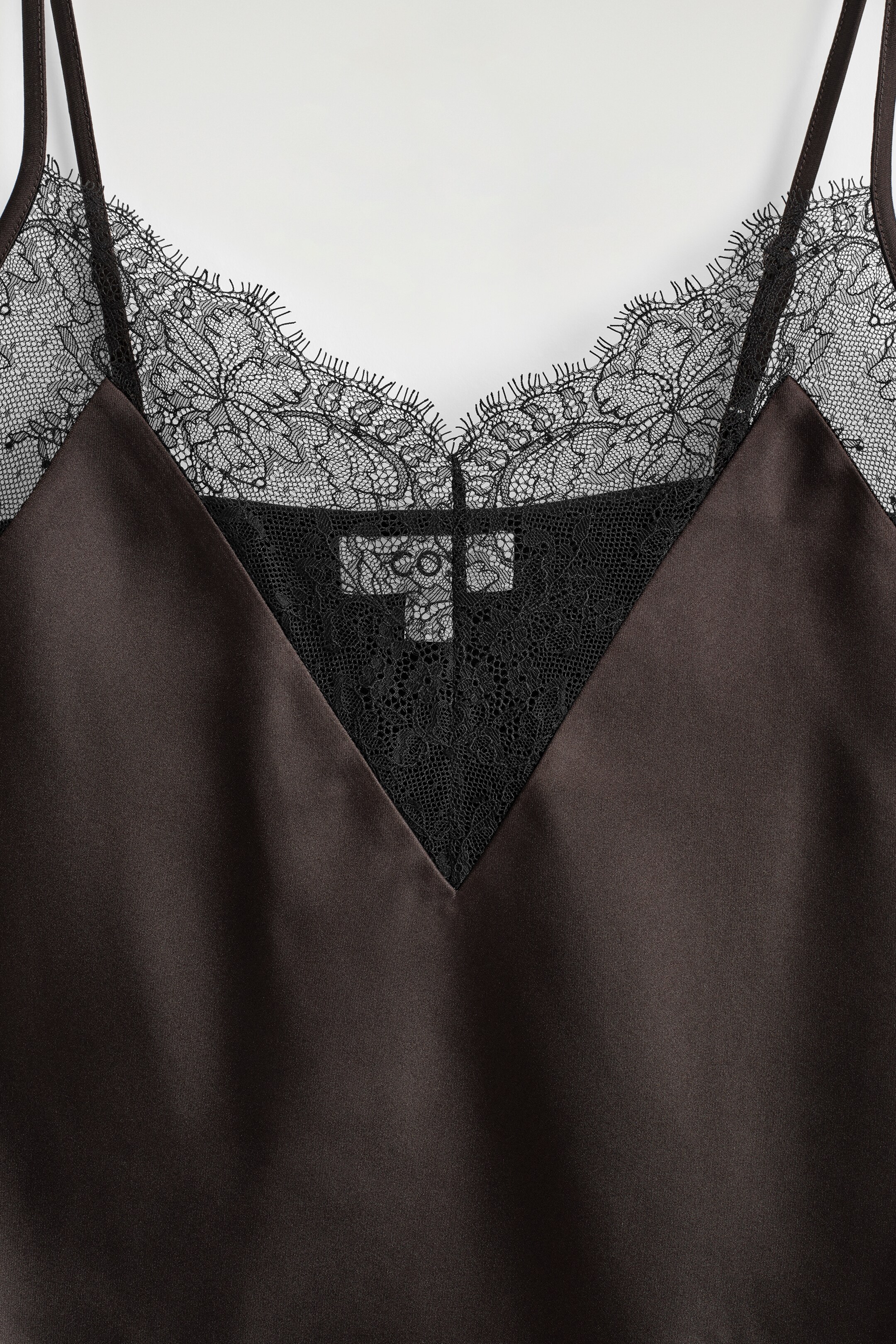 Ver imagen más grande: Una camisola de satén marrón chocolate está mostrando su parte DELANTERA, con un escote en V adornado con un delicado encaje negro. El encaje forma un borde festoneado y se extiende en un panel triangular en el centro, con finos tirantes ajustables visibles en la parte superior.
