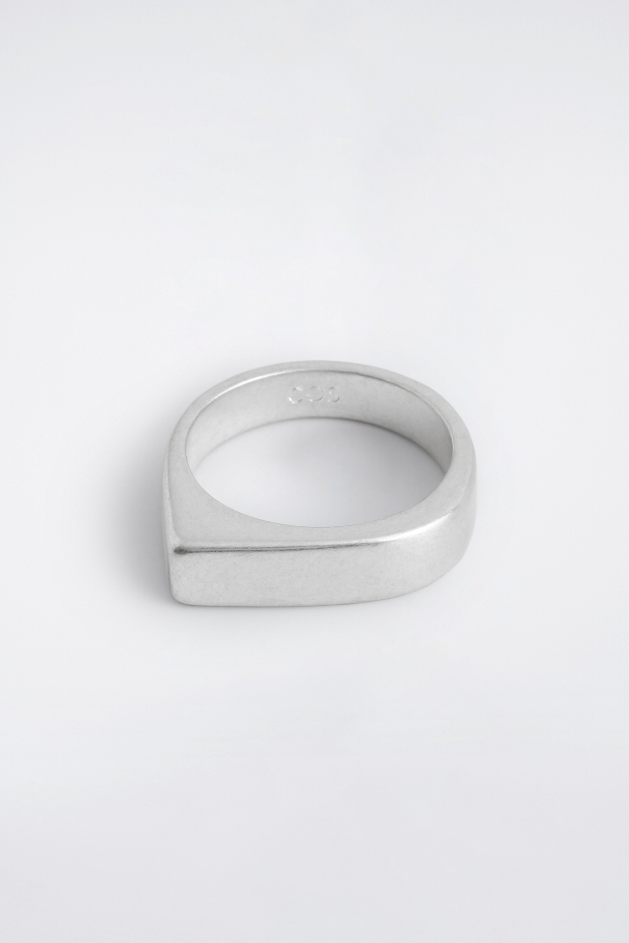 Grösseres Bild ansehen: Ein versilberter Siegelring zeigt ein skulpturales Design, bei dem die obere Fläche auf der einen Seite gebogen und auf der anderen Seite eckig ist. Der Ring weist ein mattes, subtil angelaufenes Finish auf.