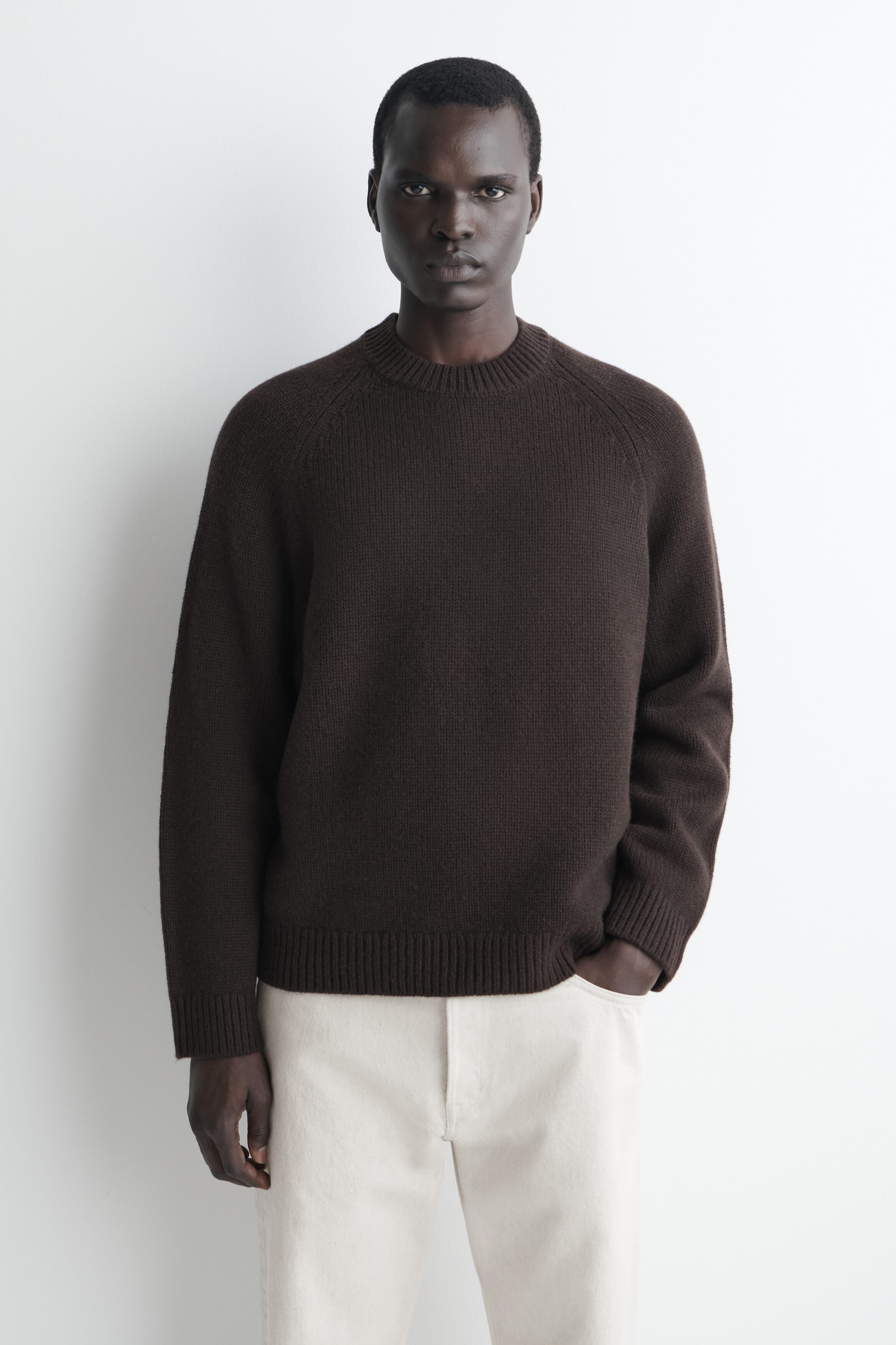 A dark brown chunky cashmere jumper is shown from the front, featuring a crew neckline, raglan sleeves, and ribbed trims on the collar, cuffs, and hem. The jumper is styled with light cream-coloured trousers, showcasing its relaxed fit. A dark brown chunky cashmere jumper is shown from the front, featuring a crew neckline, raglan sleeves, and ribbed trims on the collar, cuffs, and hem. The jumper is styled with light cream-coloured trousers, showcasing its relaxed fit.
