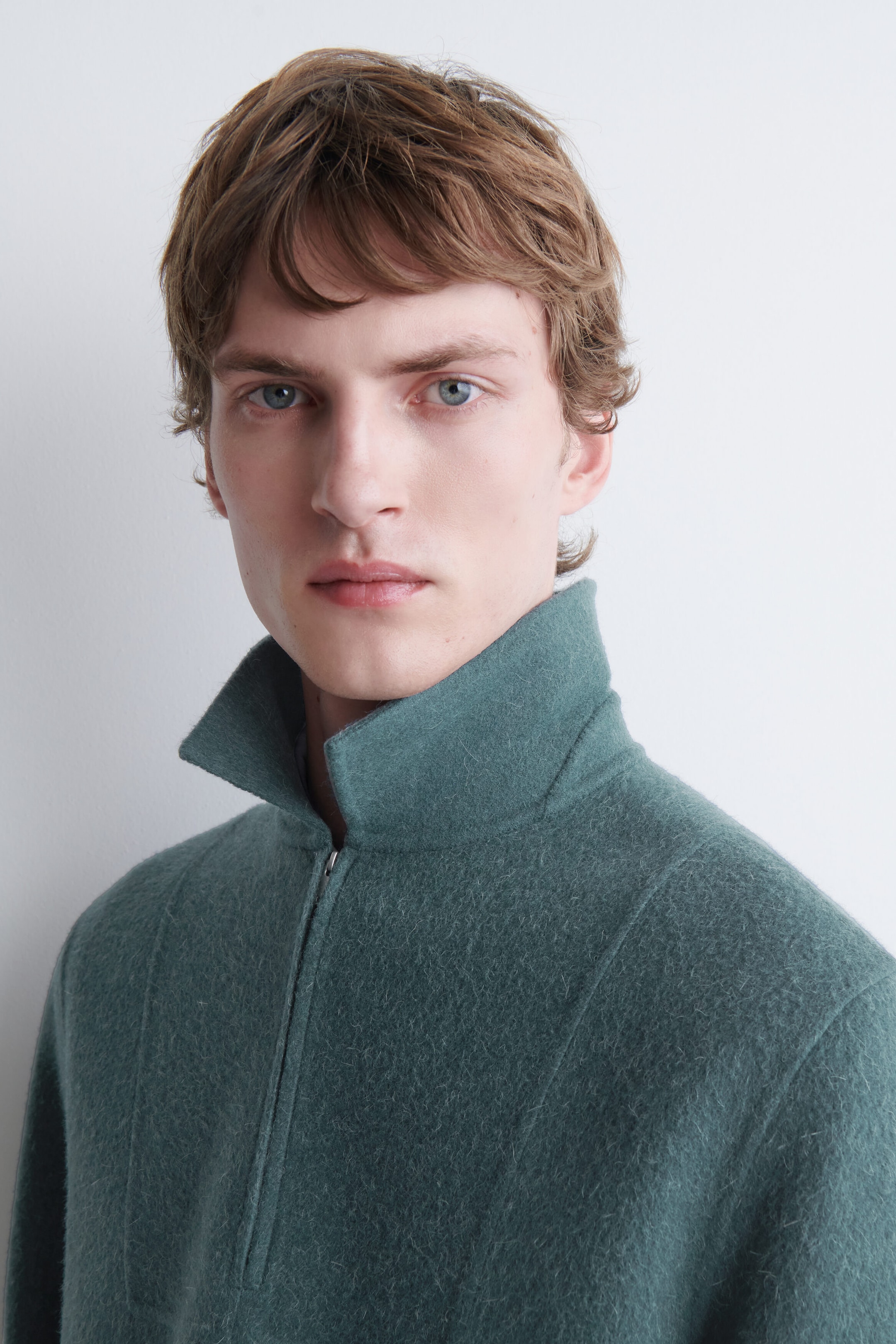 A teal-green textured wool-blend pullover featuring a high, structured stand-up collar and a partial front zipper. The garment features vertical seam detailing running down the front chest and shoulder area. A teal-green textured wool-blend pullover featuring a high, structured stand-up collar and a partial front zipper. The garment features vertical seam detailing running down the front chest and shoulder area.