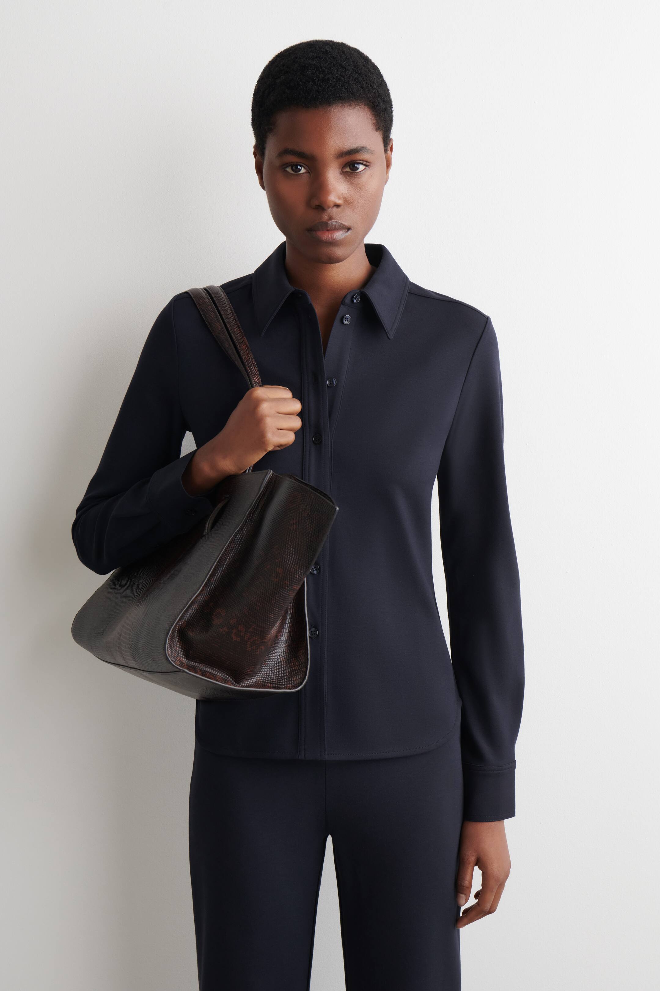 Agrandir l'image: Une chemise bleu foncé à manches longues et à boutons est présentée, avec un col pointu et une coupe lisse et ajustée. La chemise est associée à un pantalon bleu foncé assorti, les deux pièces affichant une silhouette épurée et élégante.