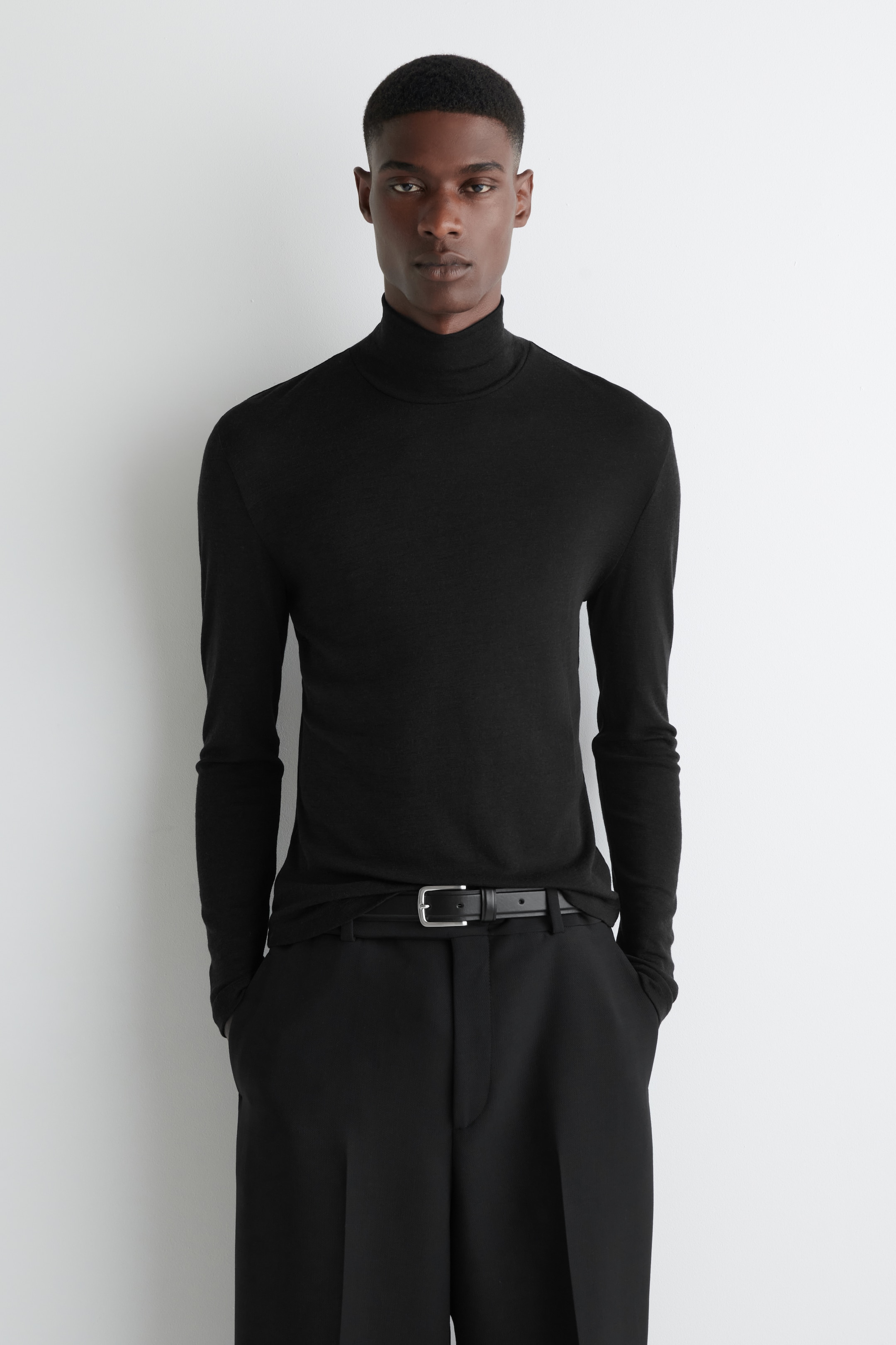 Agrandir l'image: Un haut à col roulé noir avec un col montant et des manches longues est porté par le mannequin. Le haut ajusté est assorti d'un pantalon noir et d'une ceinture noire.