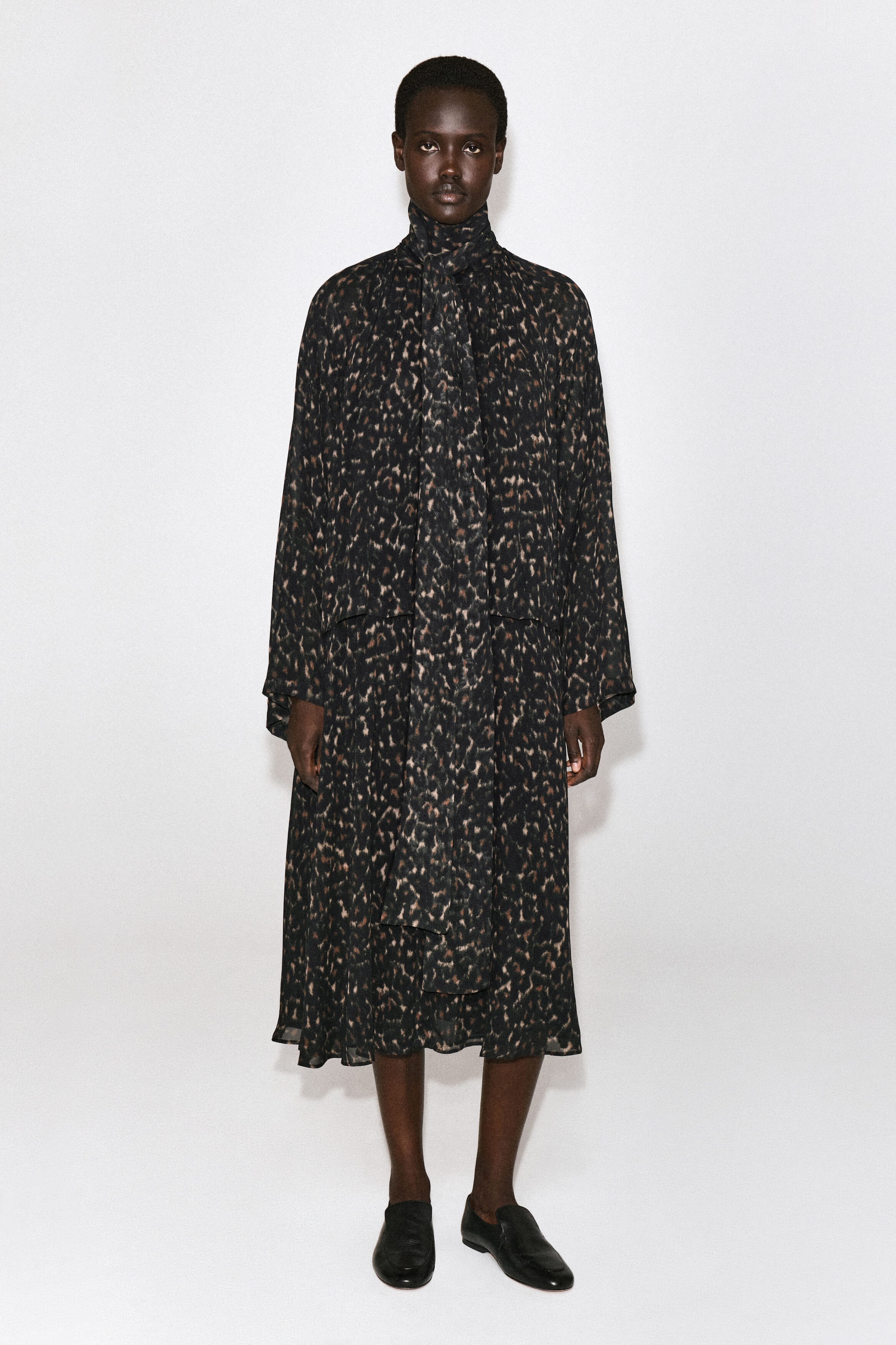 The leopard-print fluid scarf-detail dress is shown from the front, featuring an all-over dark animal print with a high neckline and an attached, draped matching scarf hanging down the centre. This midi-length dress has loose, long sleeves and a relaxed, fluid silhouette. The leopard-print fluid scarf-detail dress is shown from the front, featuring an all-over dark animal print with a high neckline and an attached, draped matching scarf hanging down the centre. This midi-length dress has loose, long sleeves and a relaxed, fluid silhouette.