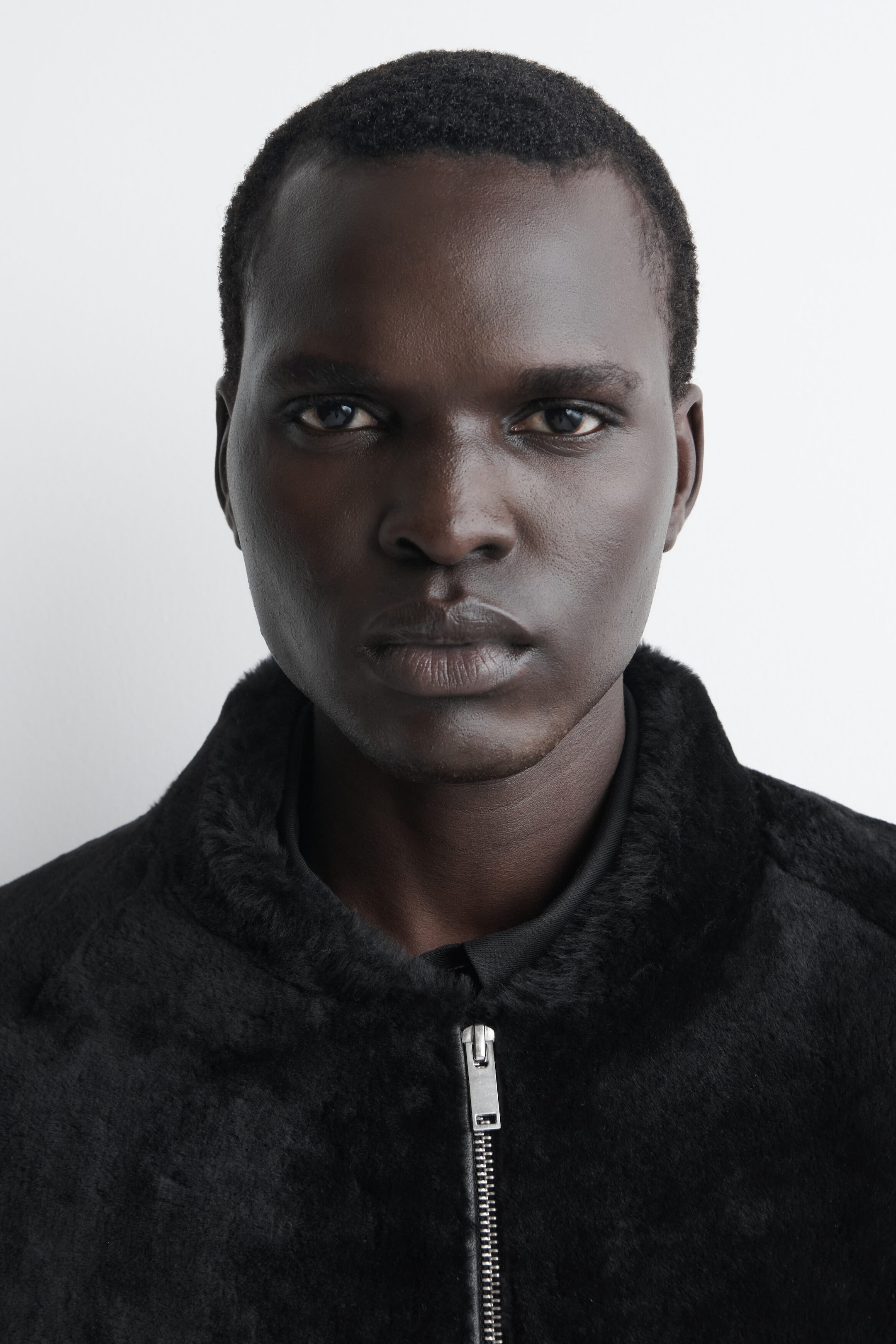 This black padded shearling bomber jacket is shown from the front in a close-up view, highlighting its plush shearling collar and a central silver zipper that is partially closed over a dark shirt collar.