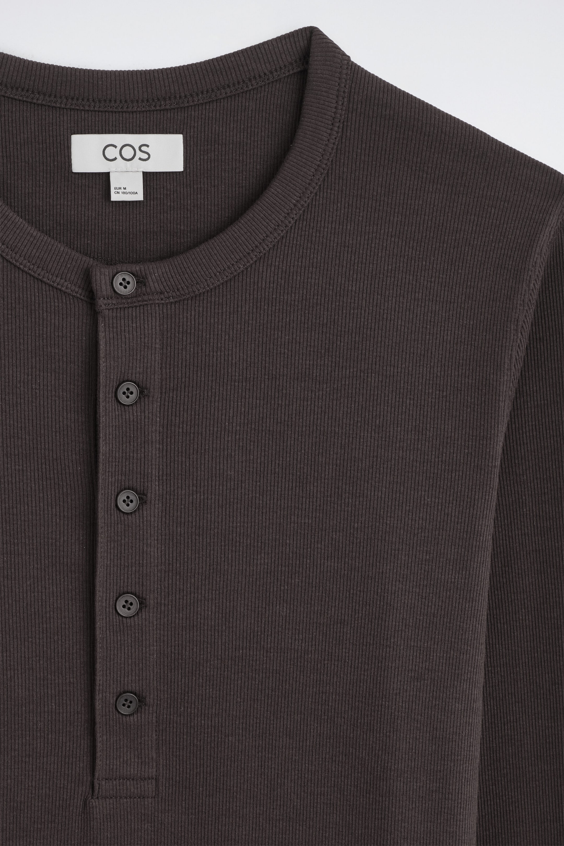 Obcisły, prążkowany bawełniany longsleeve Henley w ciemnym brązie prezentuje drobną pionową strukturę prążkowania, zaokrąglony okrągły dekolt oraz pięcioguzikową listwę w zbliżeniu od przodu. Obcisły, prążkowany bawełniany longsleeve Henley w ciemnym brązie prezentuje drobną pionową strukturę prążkowania, zaokrąglony okrągły dekolt oraz pięcioguzikową listwę w zbliżeniu od przodu.