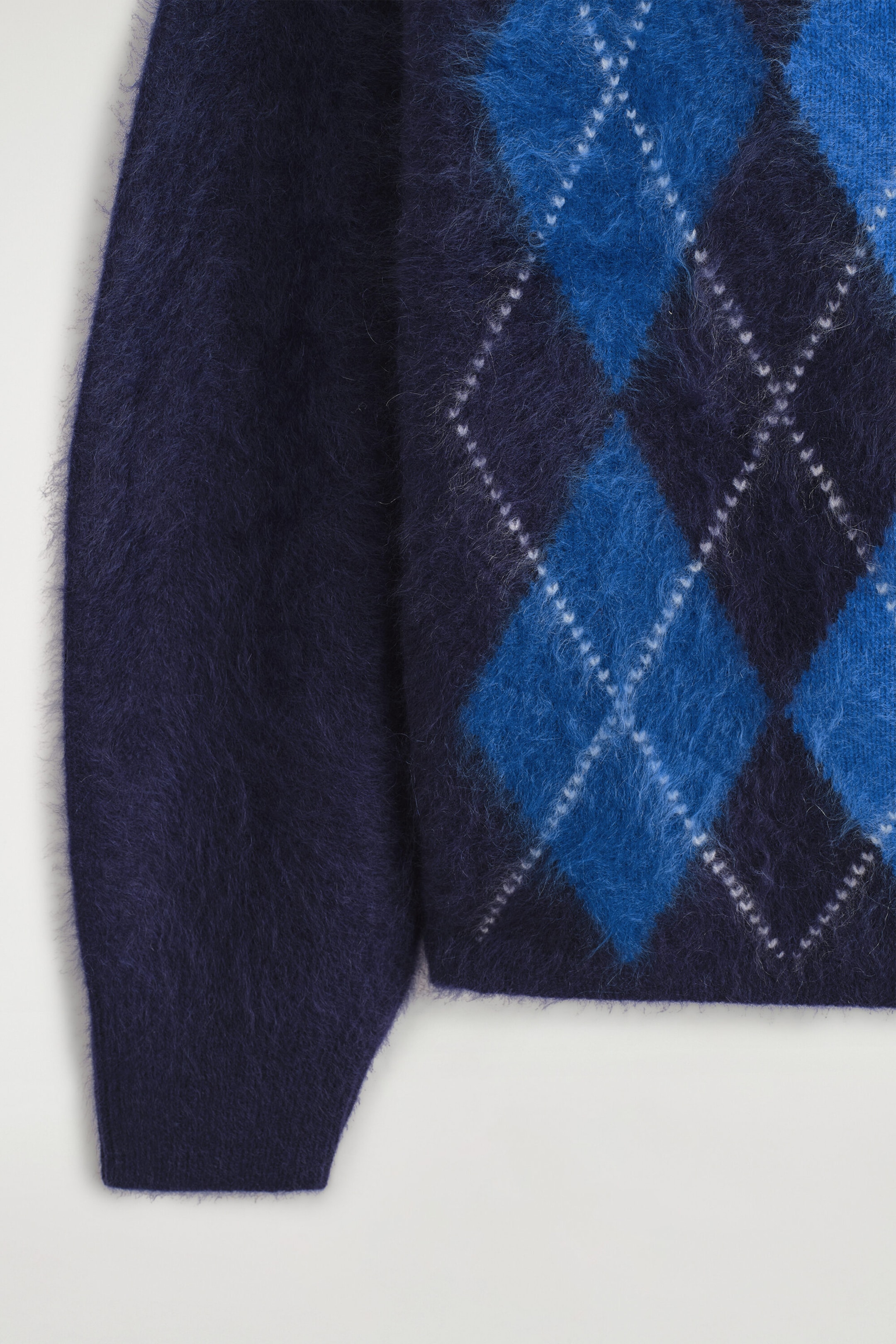 The argyle brushed pure cashmere funnel-neck jumper features a soft, brushed texture with a prominent navy and bright blue argyle pattern outlined in white stitching. This close-up front view shows a solid navy sleeve with a ribbed cuff alongside the patterned body of the garment. The argyle brushed pure cashmere funnel-neck jumper features a soft, brushed texture with a prominent navy and bright blue argyle pattern outlined in white stitching. This close-up front view shows a solid navy sleeve with a ribbed cuff alongside the patterned body of the garment.