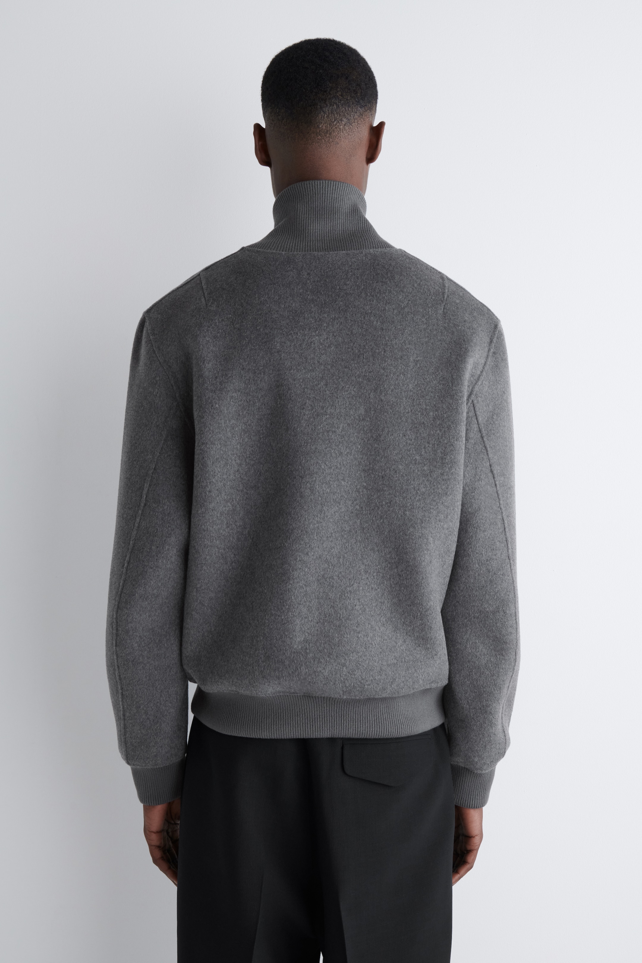 Ver imagen más grande: Una chaqueta bomber gris oscuro está siendo usada por el modelo. Presenta un cuello alto acanalado, puños acanalados y un dobladillo acanalado, y está combinada con pantalones negros.
