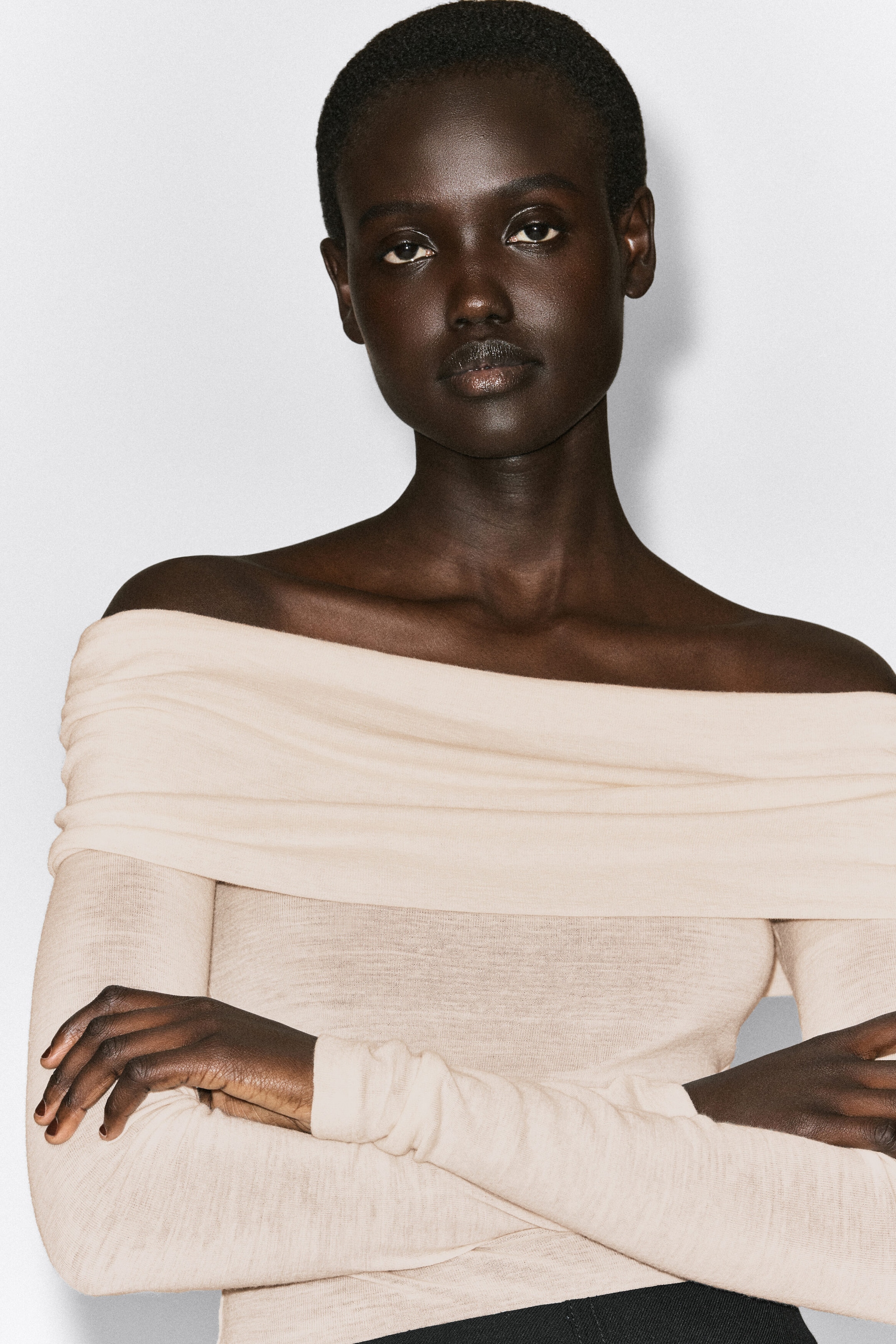 This cream-colored off-the-shoulder merino wool top is shown from the front, featuring a wide, folded-over neckline that drapes straight across the shoulders. The long-sleeved, fine-knit top fits close to the body, highlighting its soft, slightly sheer texture. This cream-colored off-the-shoulder merino wool top is shown from the front, featuring a wide, folded-over neckline that drapes straight across the shoulders. The long-sleeved, fine-knit top fits close to the body, highlighting its soft, slightly sheer texture.