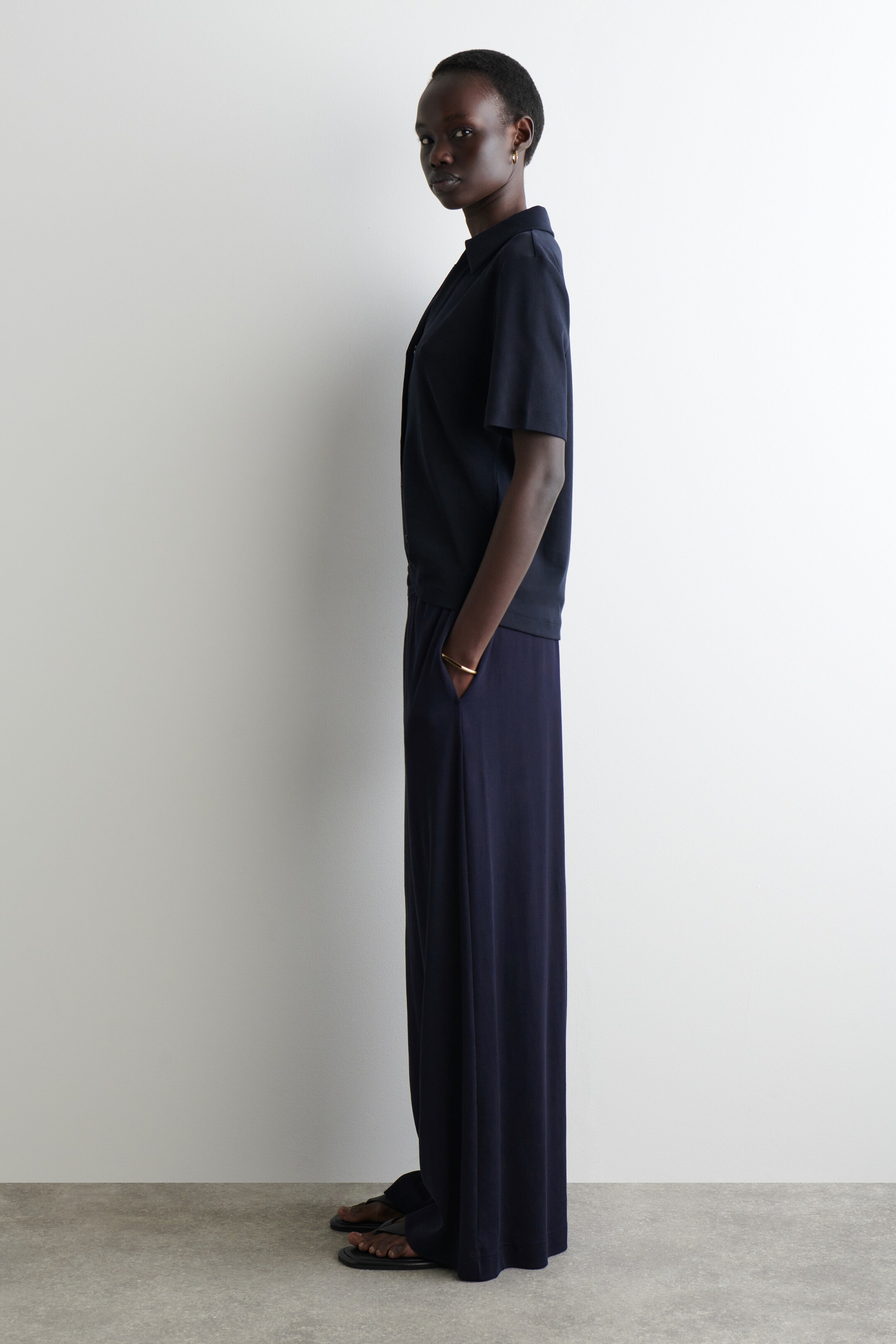 Agrandir l'image: Un haut à col bleu foncé à manches courtes et un pantalon large assorti sont présentés de profil. Le haut présente une coupe décontractée, et le pantalon long tombe de manière ample.