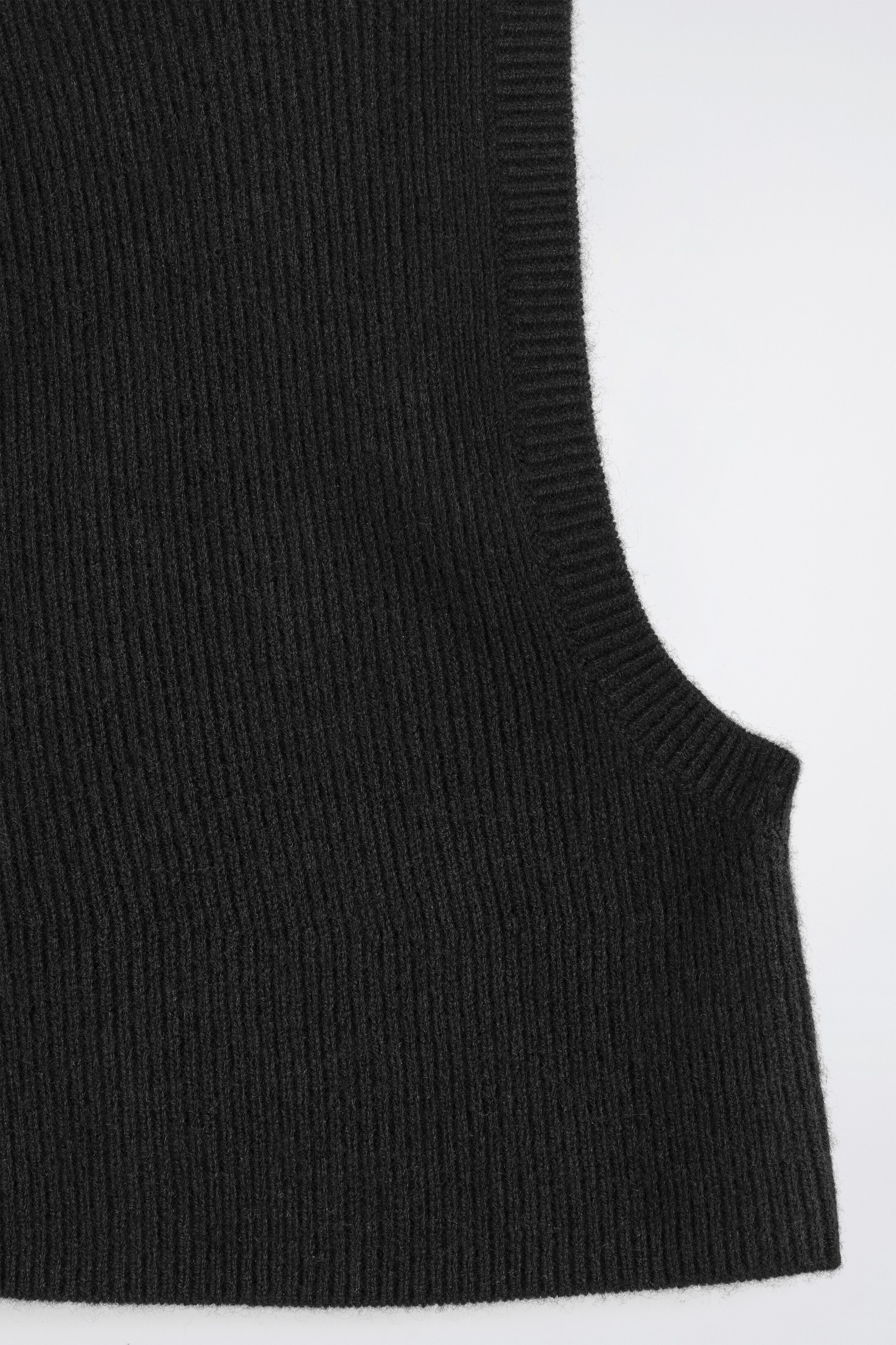 View larger image: A close-up view is showing a section of a black balaclava, featuring a ribbed knit texture with vertical ribs throughout, and a curved opening finished with a tighter ribbed trim.