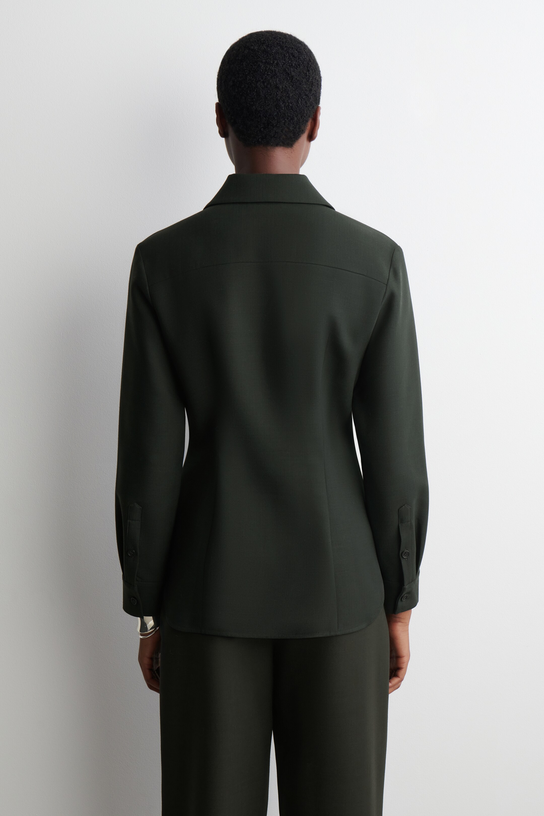 Grotere afbeelding bekijken: Een donkergroen shirt met lange mouwen wordt van de achterkant gepresenteerd, waarbij de rechte pasvorm wordt getoond. Het heeft een standaardkraag, een zichtbare rugpas en knoopmanchetten.