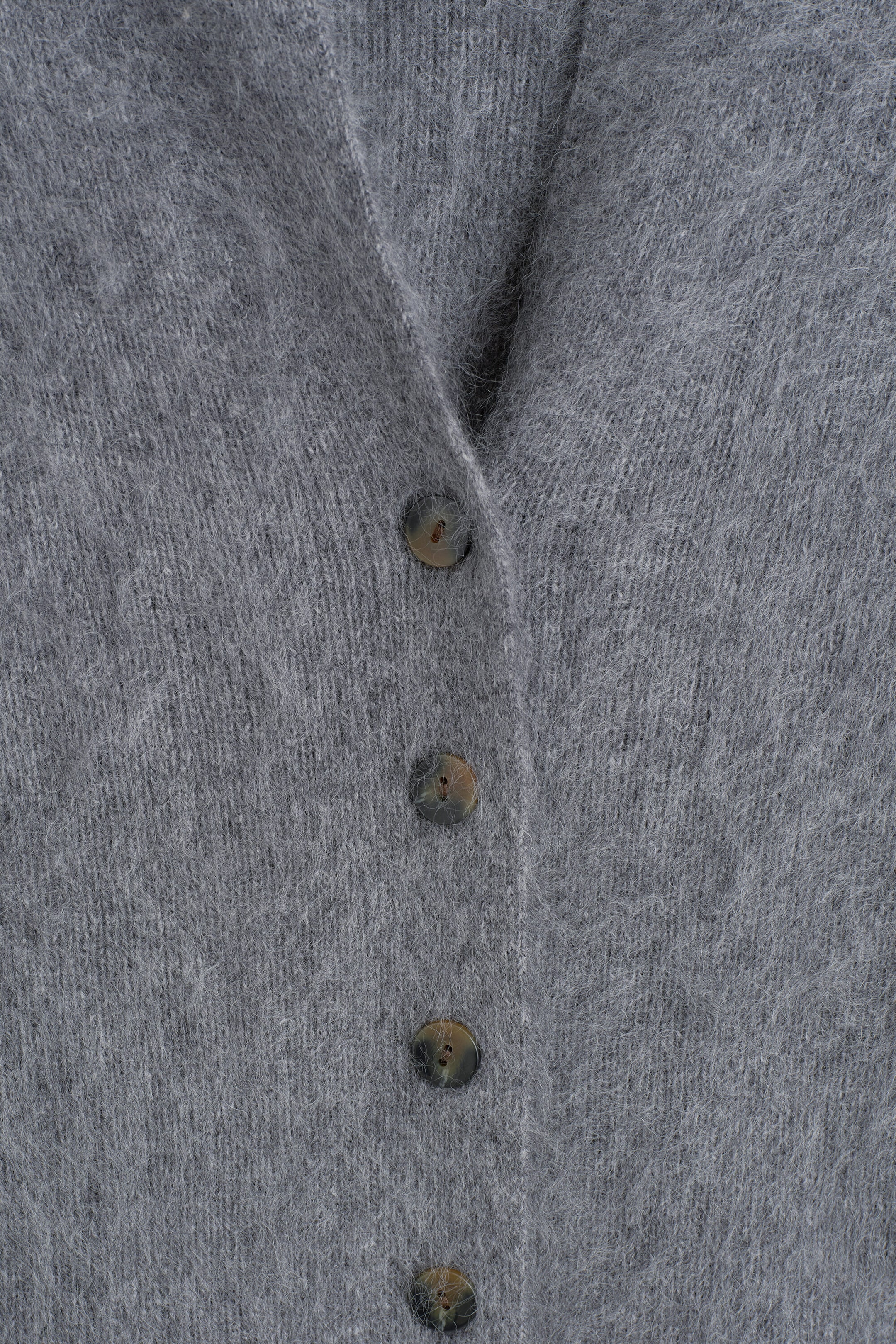 The DRAPED BRUSHED MERINO WOOL CARDIGAN is shown with its front button placket, highlighting its soft, fuzzy, brushed gray knit texture. Four mottled brown tortoiseshell buttons fasten the cardigan down the center.