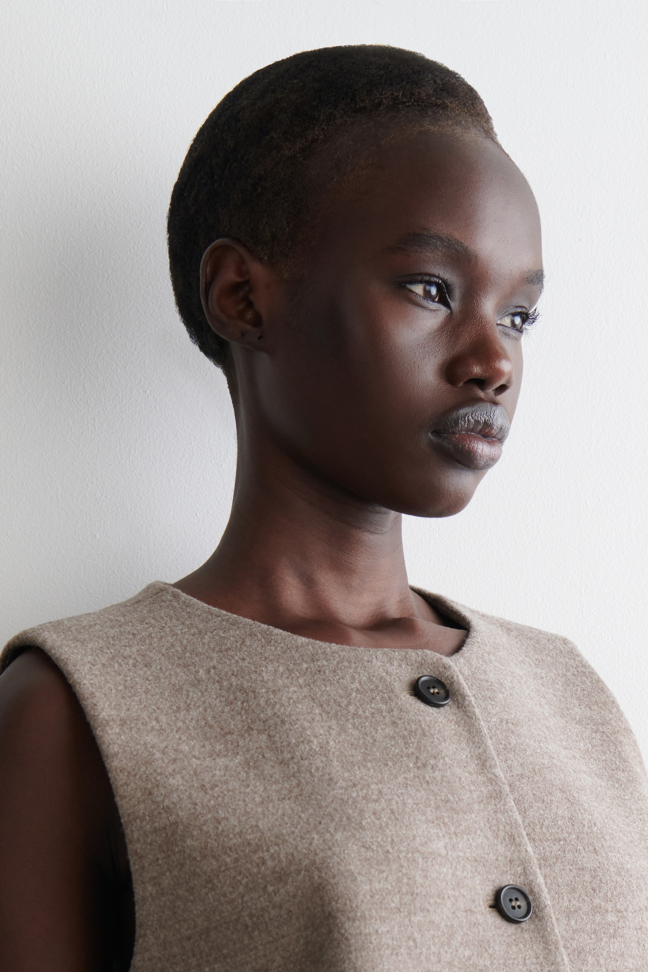 View larger image: A light brown, sleeveless waistcoat is being worn, showing its upper front. It is featuring a rounded neckline and a textured, boiled wool blend fabric, with two visible dark buttons closing the front.