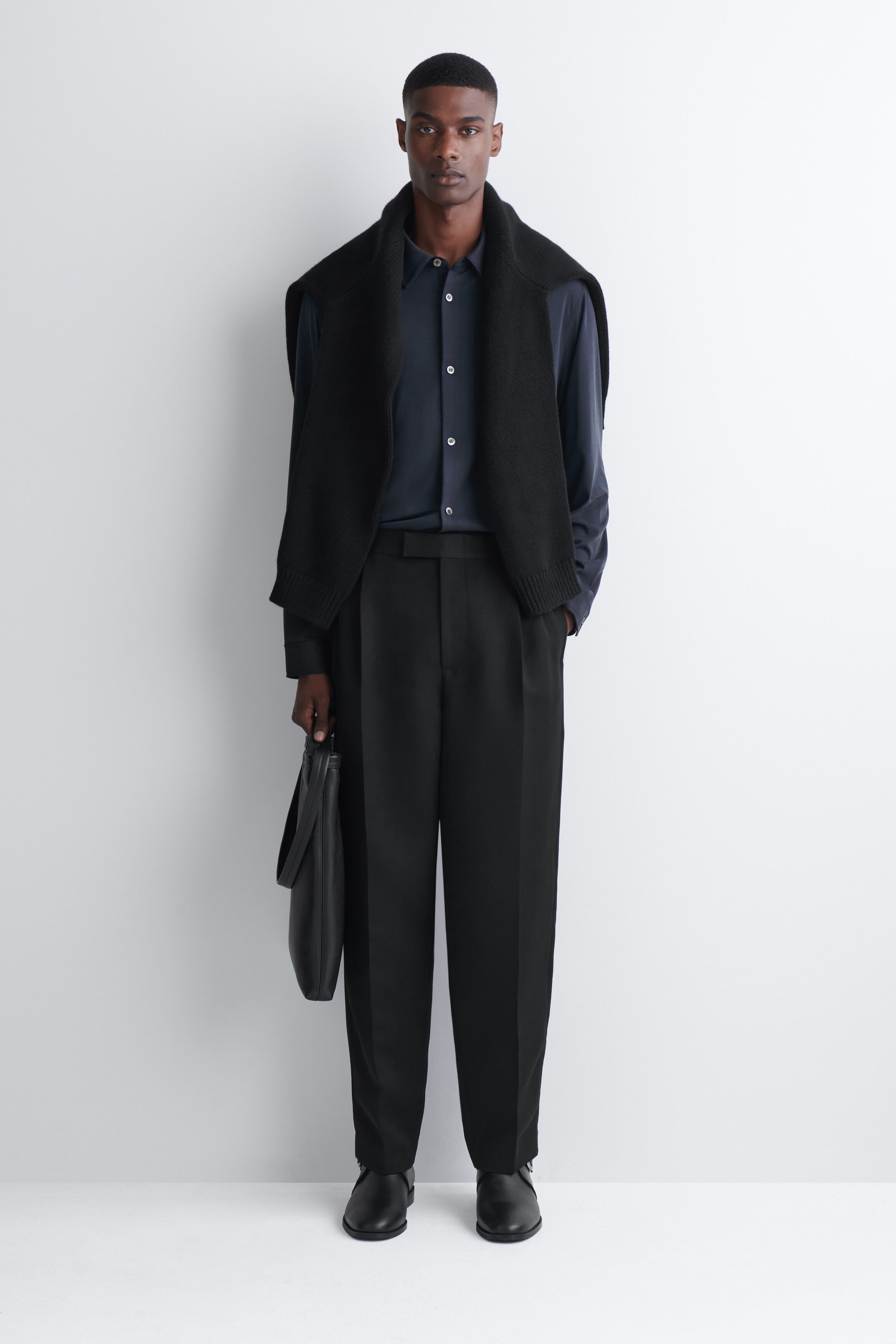 The fluid interlock jersey shirt in dark navy is worn by the model, tucked into tailored black trousers and styled with a black knit sweater draped over the shoulders. The long-sleeve shirt features a pointed collar and contrasting light-colored button closures down the front. The fluid interlock jersey shirt in dark navy is worn by the model, tucked into tailored black trousers and styled with a black knit sweater draped over the shoulders. The long-sleeve shirt features a pointed collar and contrasting light-colored button closures down the front.