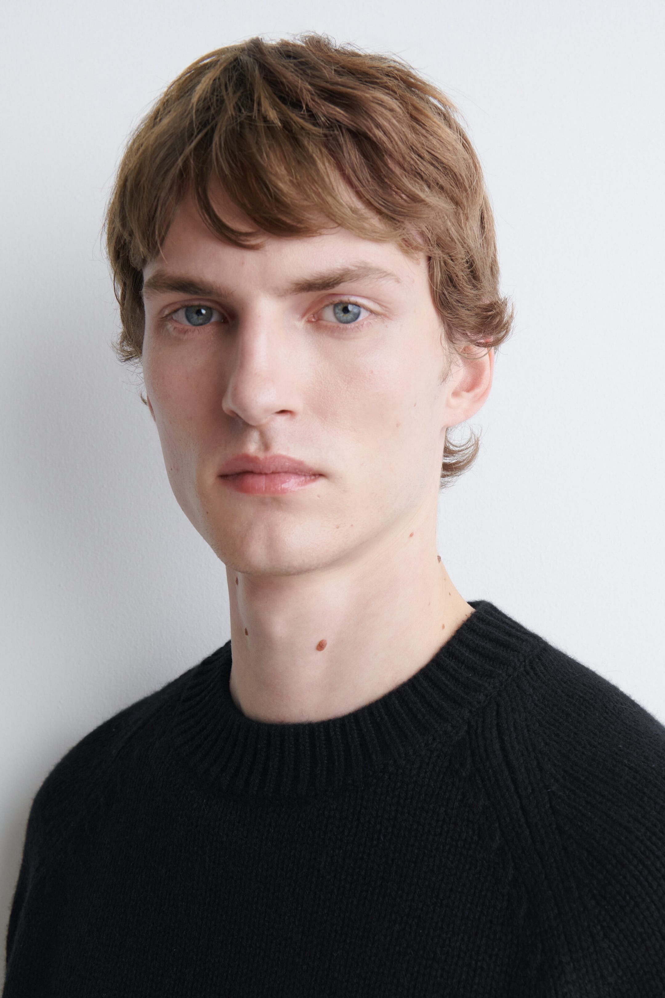 The model is wearing a black knitted jumper with a ribbed crew neck. The close-up view highlights the fabric texture and neckline. The model is wearing a black knitted jumper with a ribbed crew neck. The close-up view highlights the fabric texture and neckline.