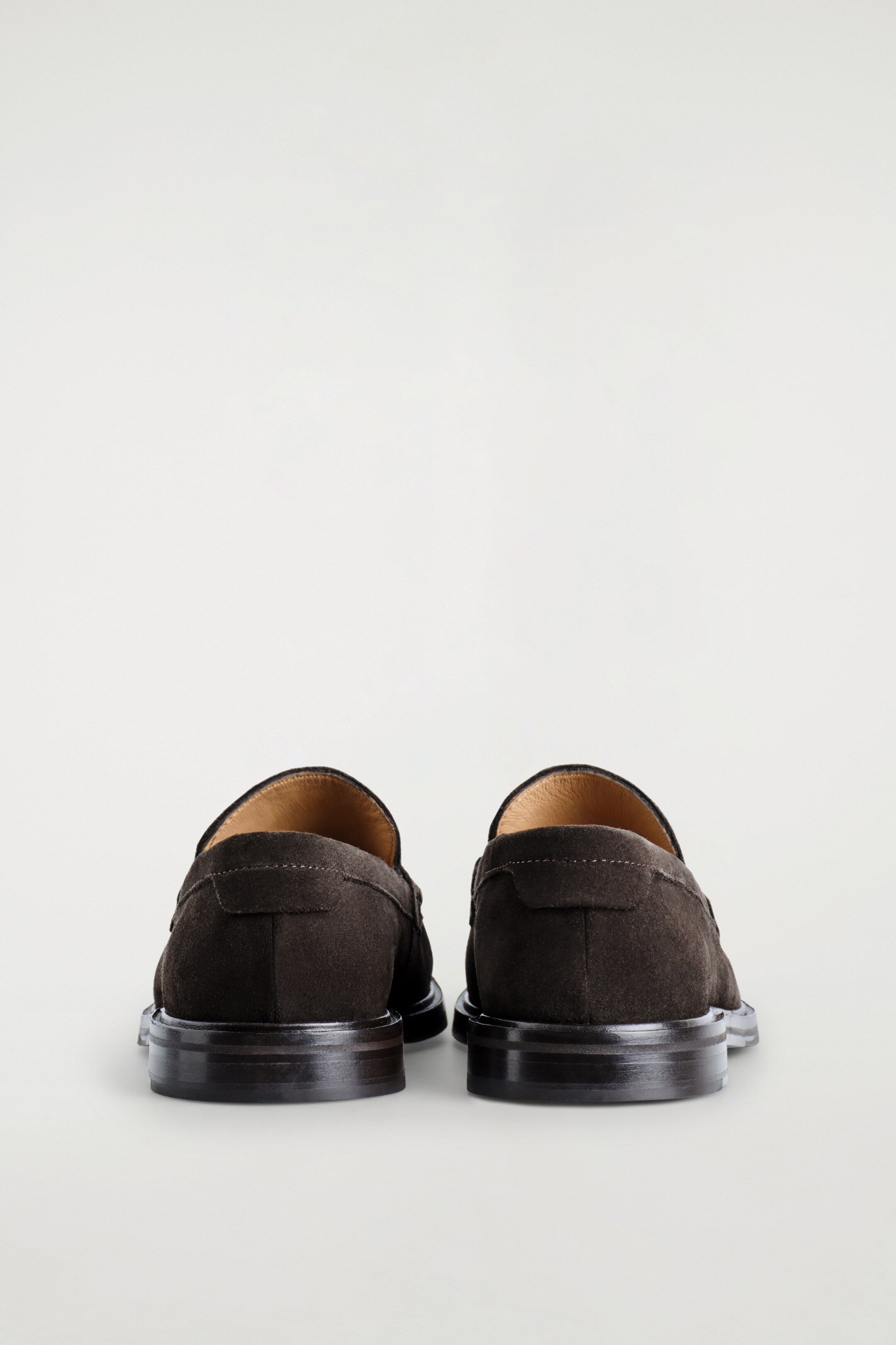 Agrandir l'image: Une paire de mocassins en daim brun foncé est placée côte à côte, présentant leur vue arrière. Ils sont dotés de talons empilés robustes et de surpiqûres ton sur ton sur les contreforts des talons.