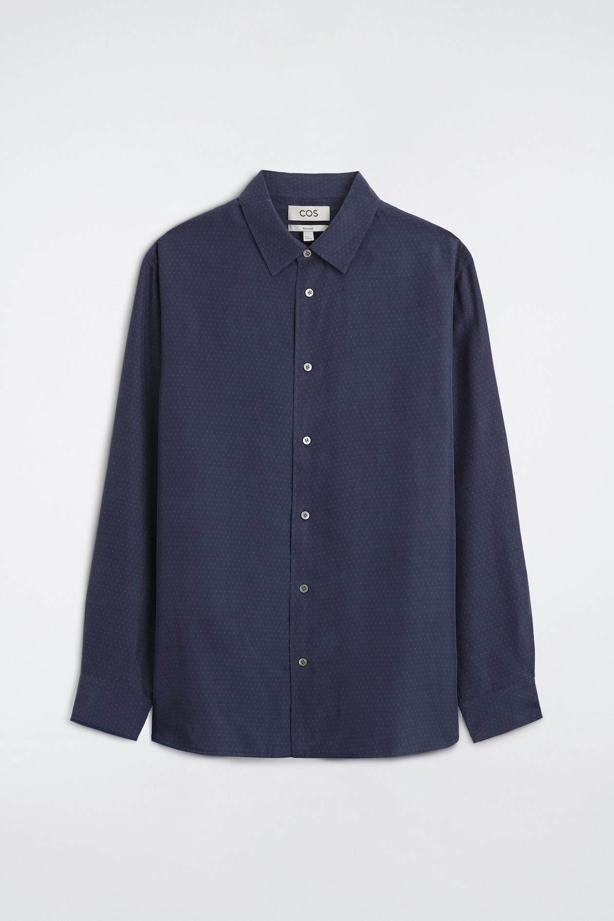 A navy blue sandwashed silk shirt is facing forward, showing a subtle all-over white micro-dot pattern. The shirt features a classic point collar, a central button-down closure with light-colored buttons, and long sleeves with structured cuffs.