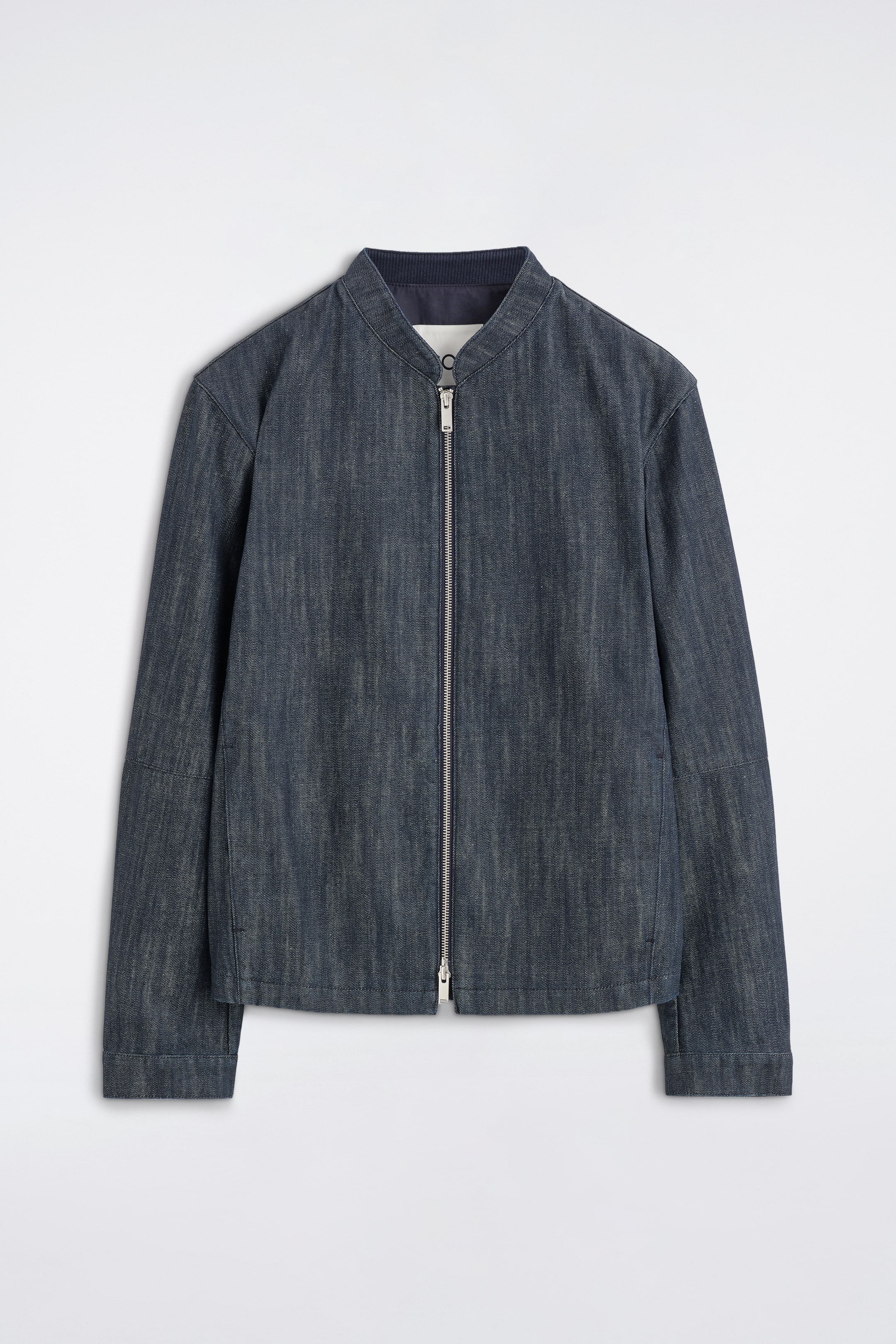 Agrandir l'image: Une veste bomber en denim bleu foncé est présentée de face, avec une fermeture éclair argentée à double sens et un col interne côtelé. La veste est coupée dans une coupe régulière, affichant des coutures discrètes et profilées sur le corps et les manches.